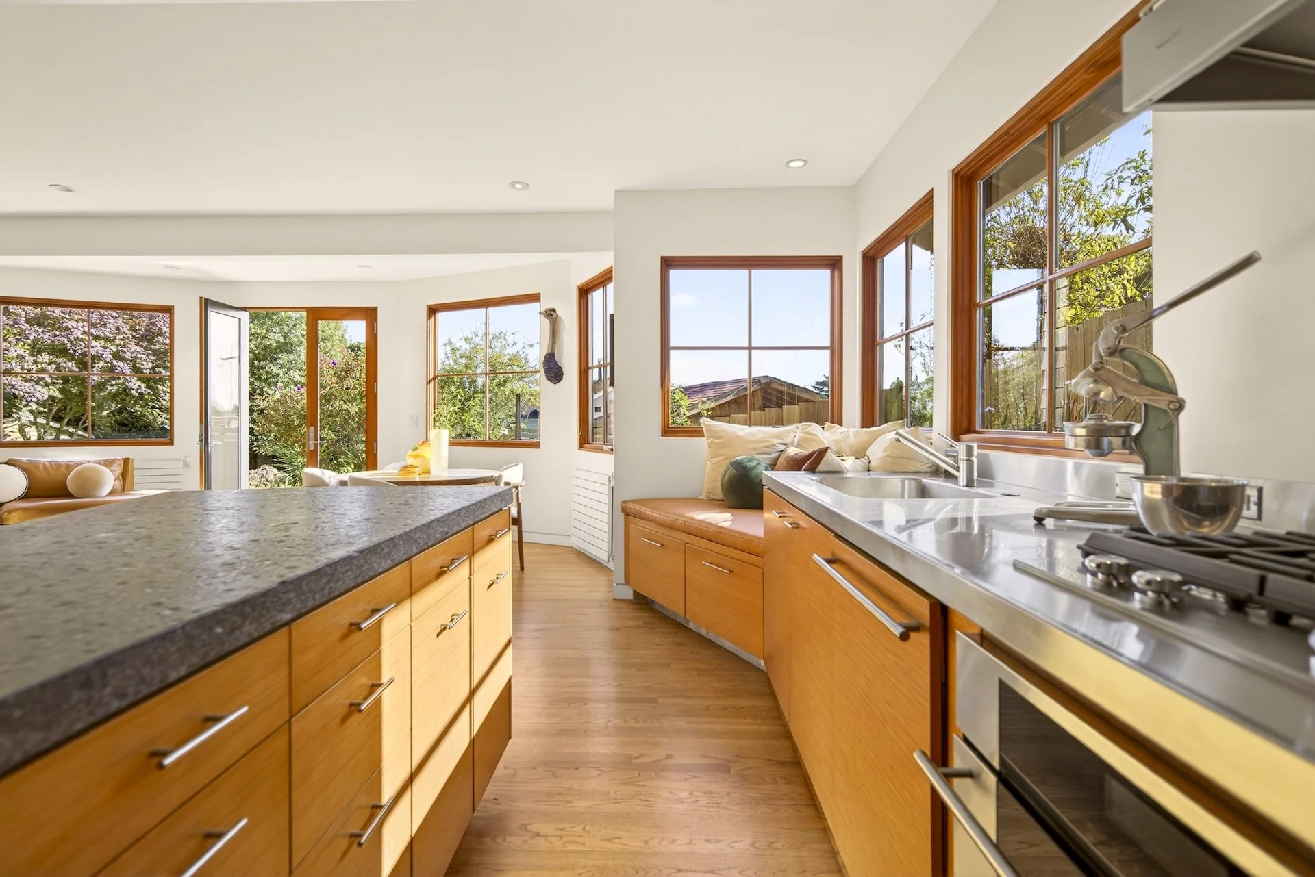 Bright kitchen with large windows, wooden cabinets, marble countertops, and a view of trees outside.