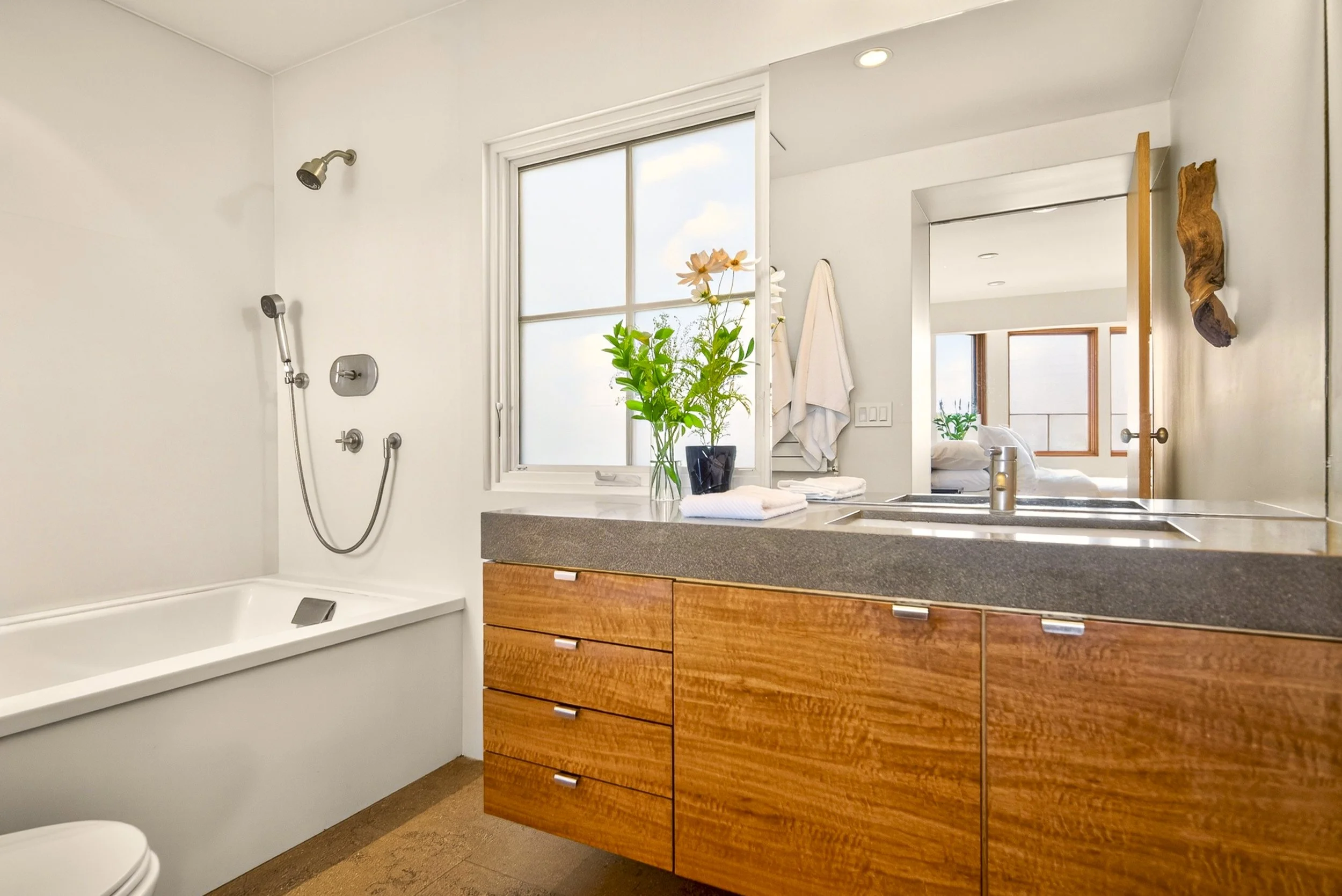 Bathroom with shower, toilet, wooden vanity with drawers, white towels, plant, and mirror.