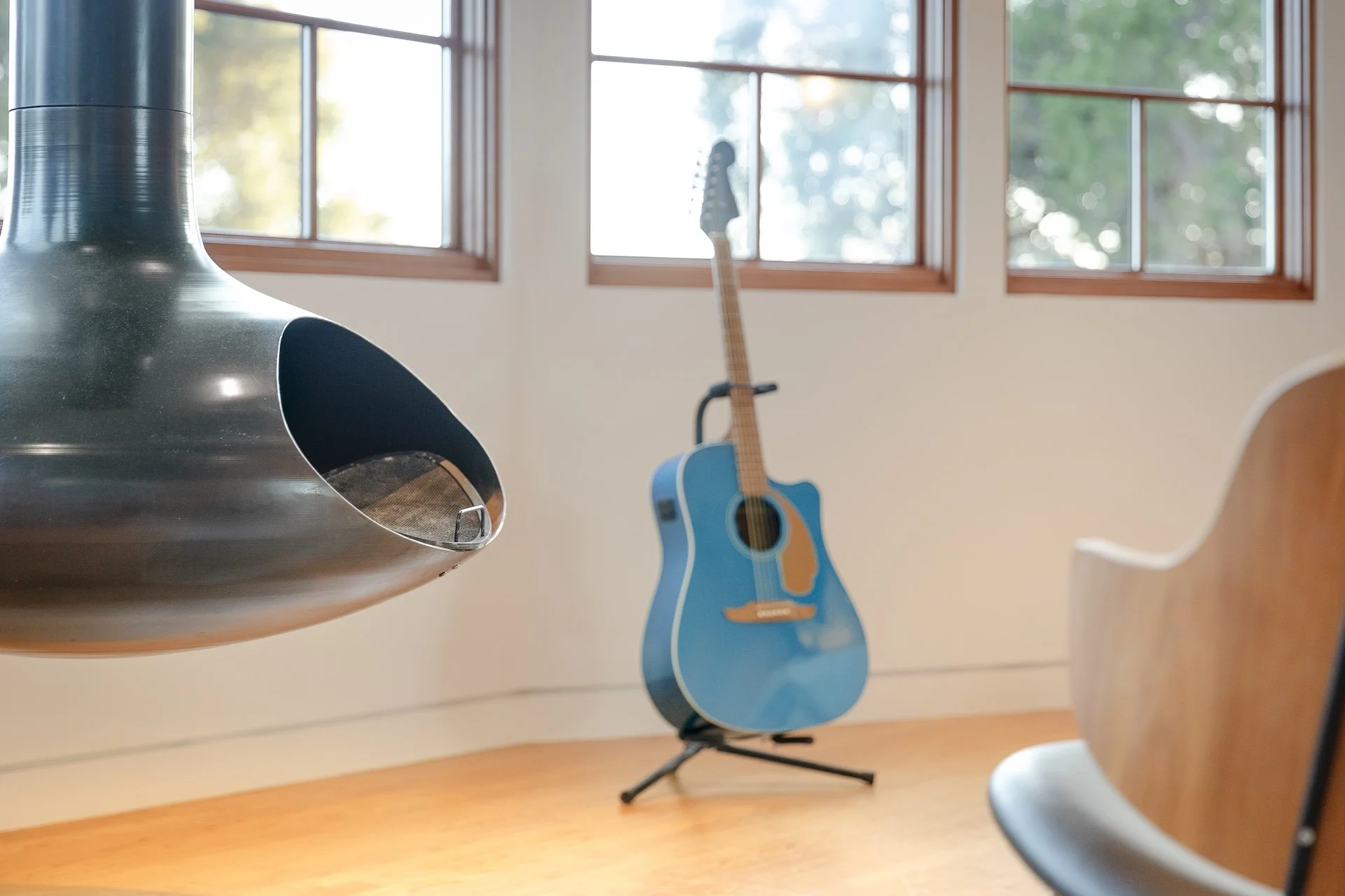A room with large windows, a blue acoustic guitar on a stand, and a black acoustic guitar hanging on the window.