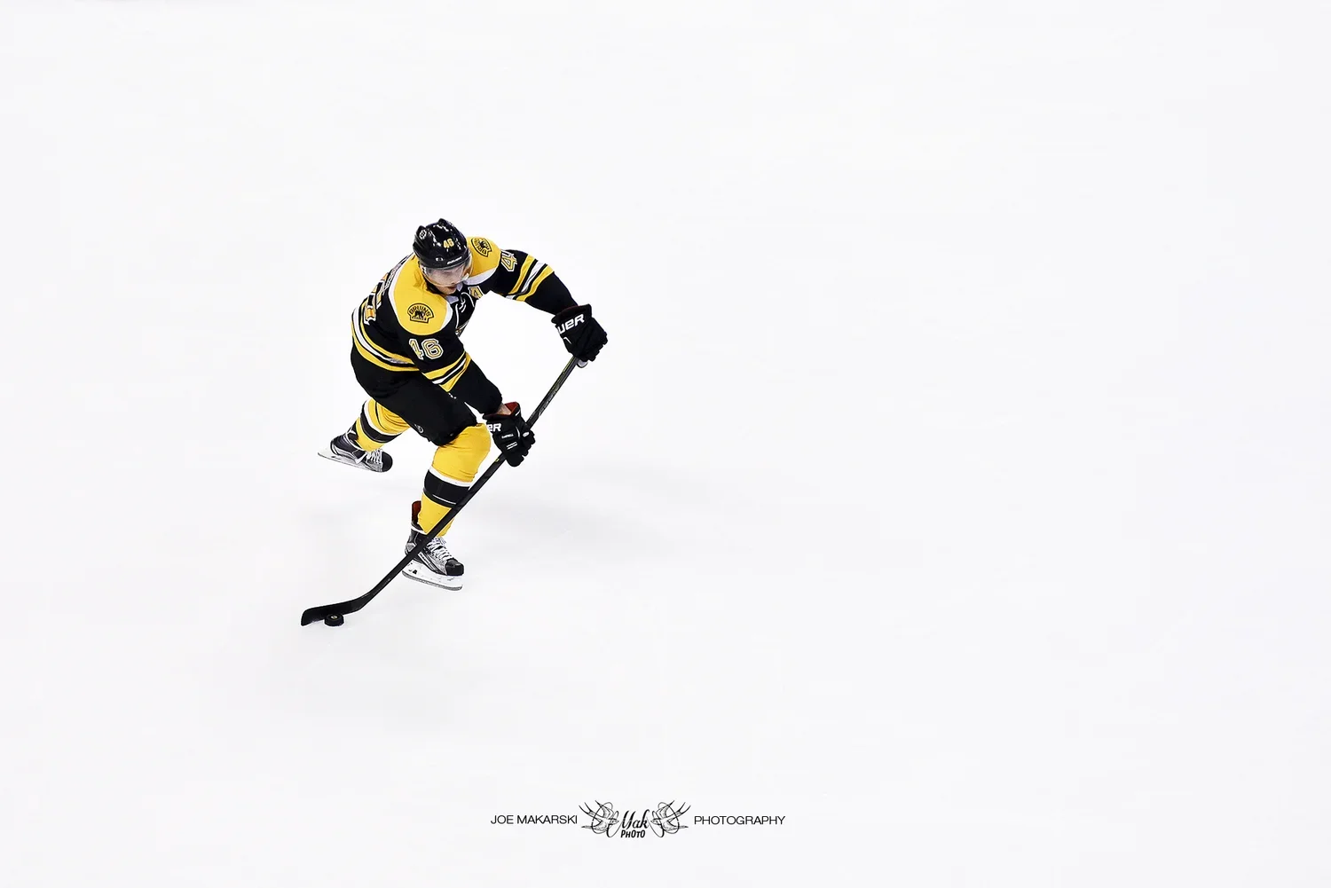 Hockey player in black and yellow uniform skating on ice with a hockey stick.