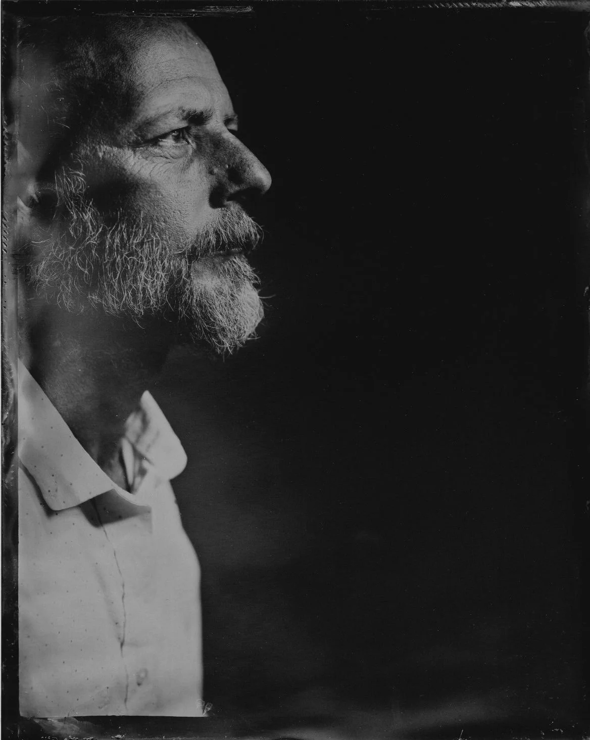 Black and white photo of an elderly man with a beard and mustache, looking to the right, with a solemn expression.