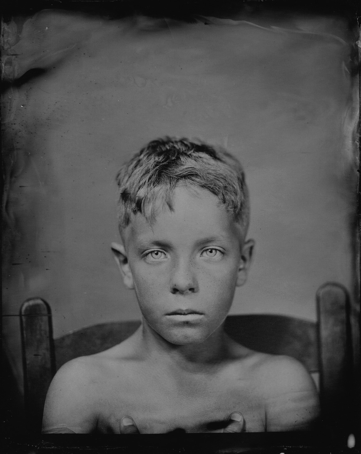 Black and white portrait of a young boy with short, tousled hair and piercing eyes, sitting on a chair.