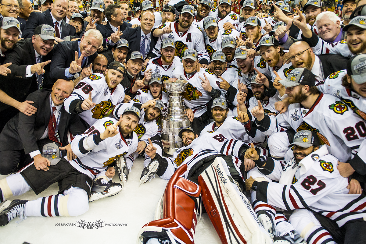 Hockey players and team staff celebrating with the Stanley Cup trophy after winning the championship.
