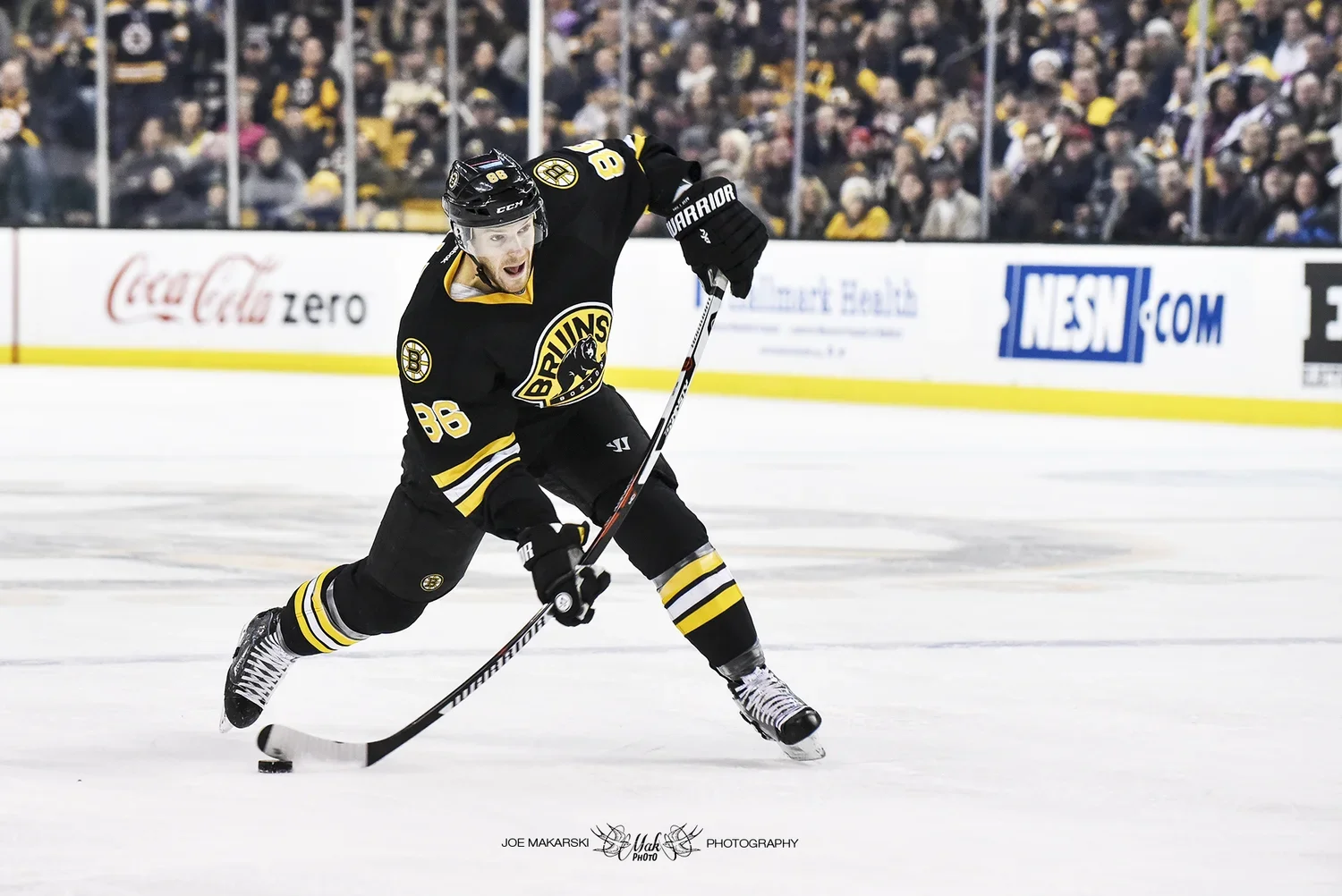 A hockey player in a black jersey with yellow accents, number 86, playing on an ice rink with a crowd in the background.