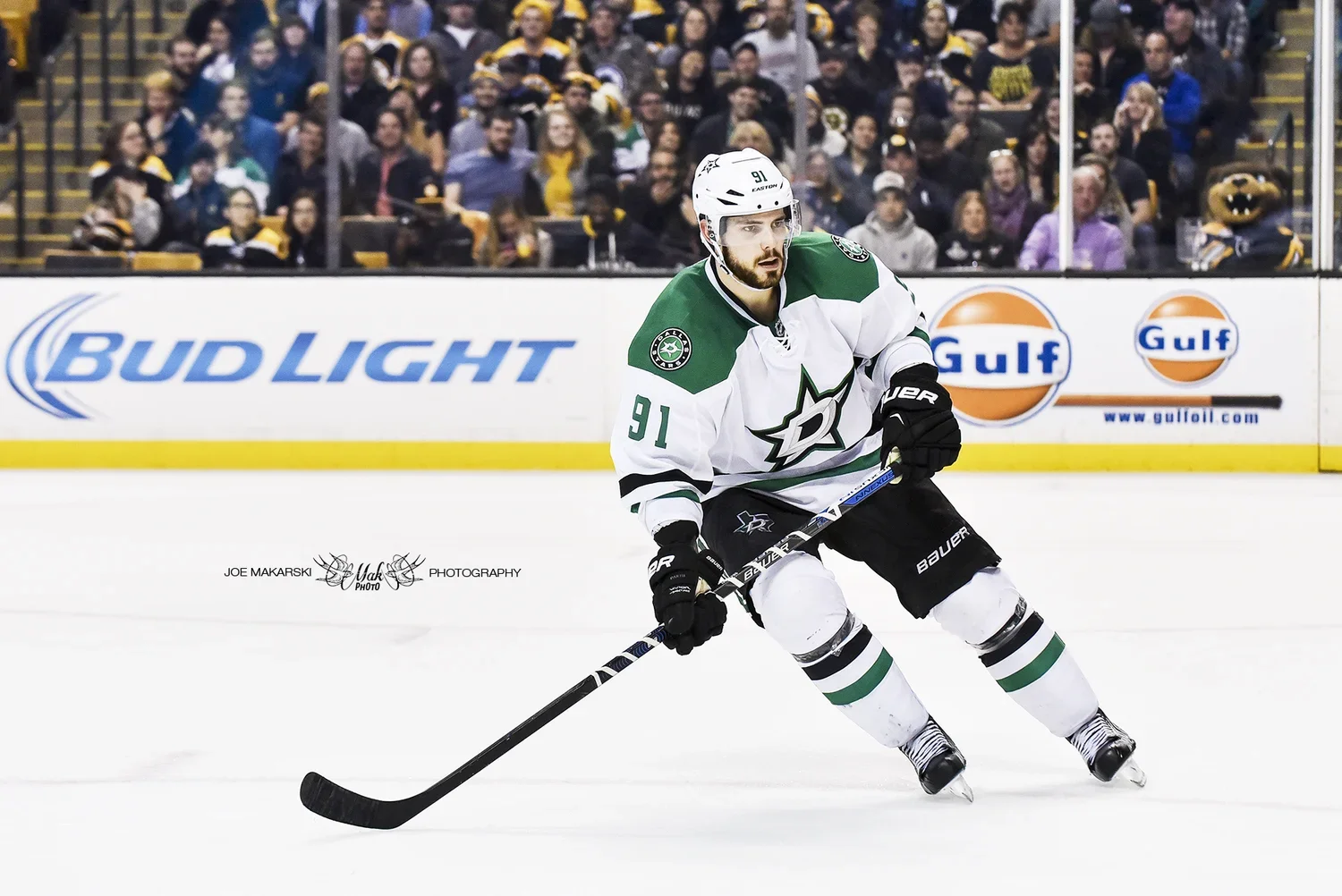 An ice hockey player in a Dallas Stars jersey skating on the ice during a game, with spectators in the background.