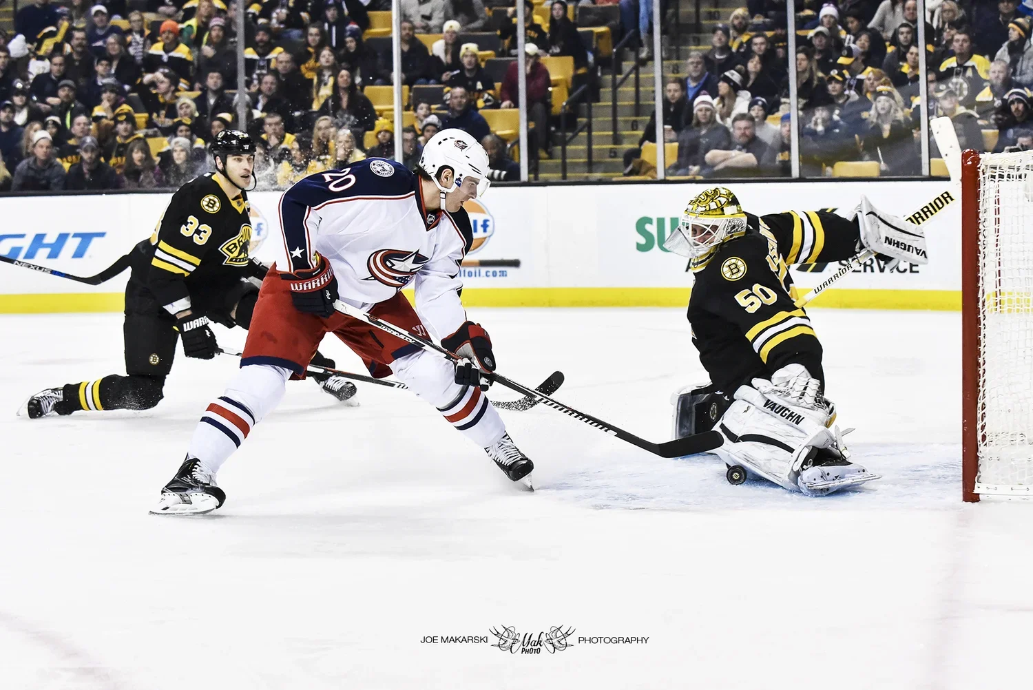 An ice hockey game with players from the Columbus Blue Jackets and Boston Bruins, where a Blue Jackets player is shooting the puck while a Bruins goalie is blocking the shot.