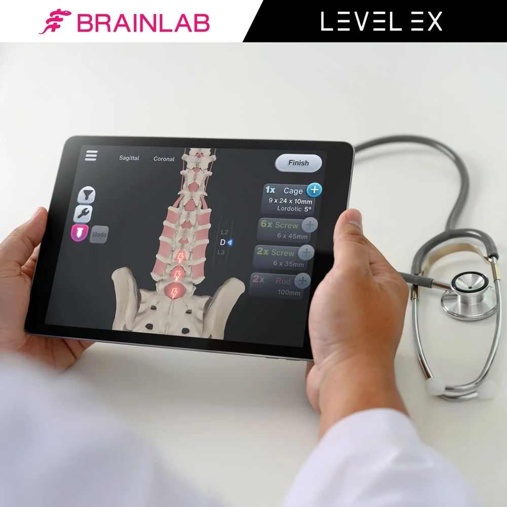 Person holding a tablet displaying a digital interface of a human spine with options for the number of screws and rods to use for spinal surgery. The tablet shows a 3D model of the spine on a black background. There is a stethoscope on a white surface next to the tablet.