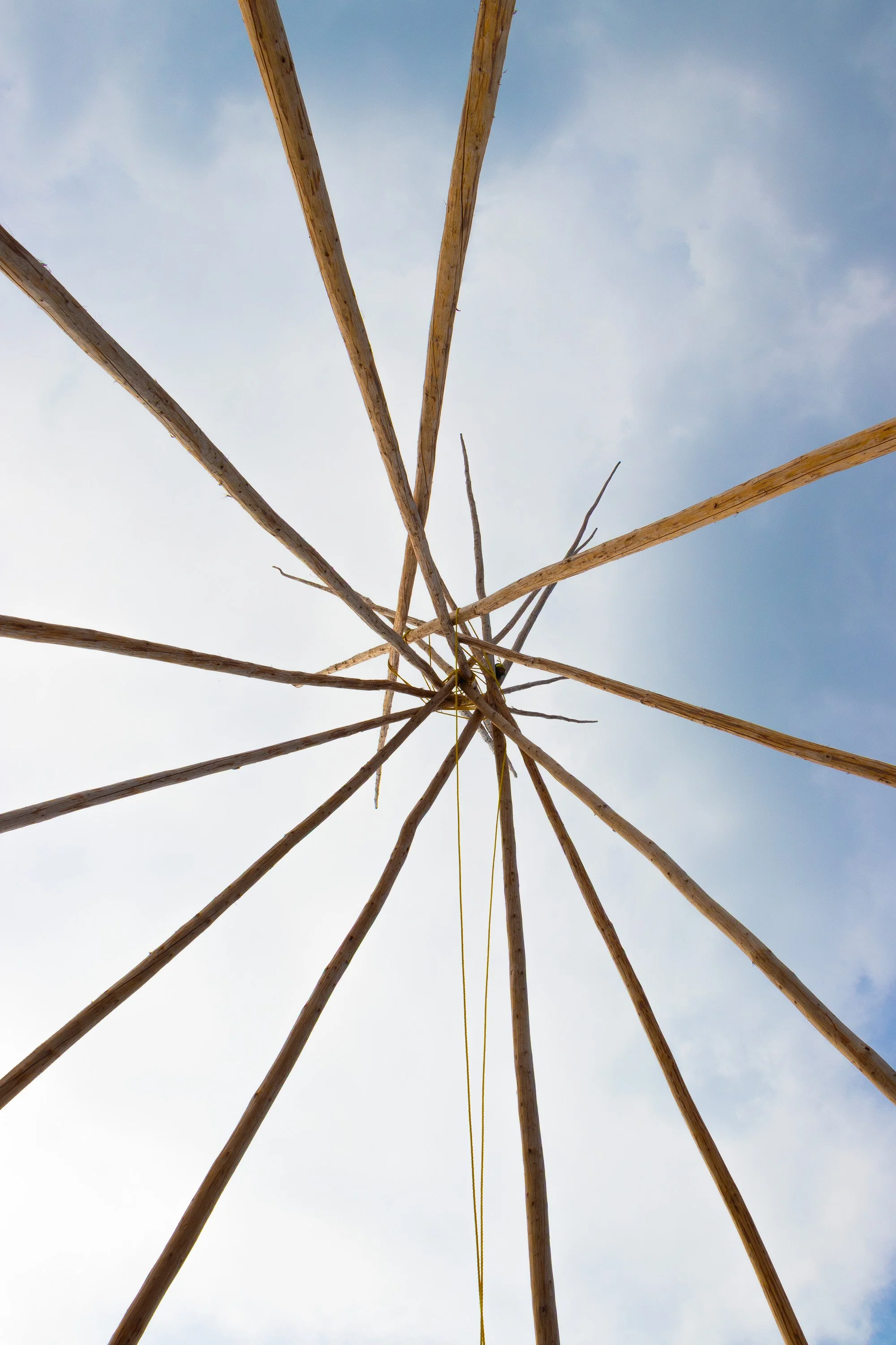 Looking up at a wooden structure, possibly a homemade tower or frame, against a cloudy sky.