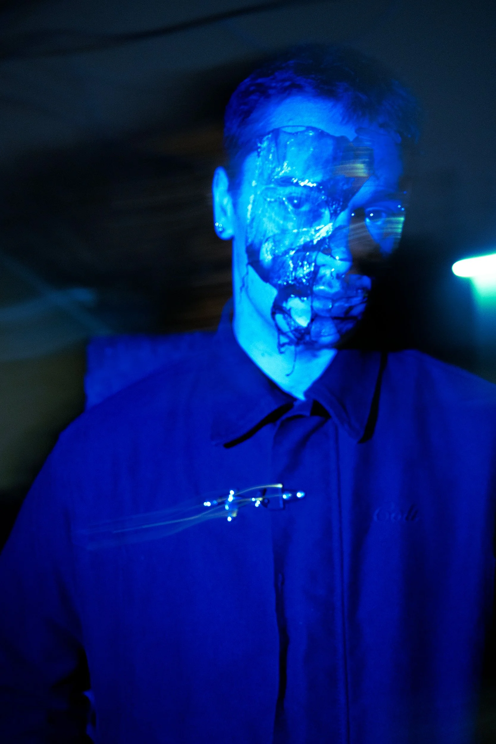A person wearing a transparent face mask illuminated with blue light, standing in a dark setting.