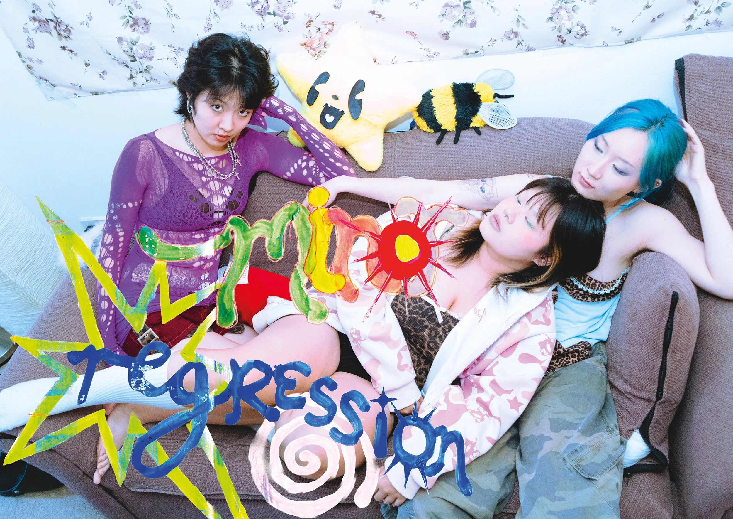 Three young women with dyed hair and tattoos lying on a couch with colorful art and decorations around them.