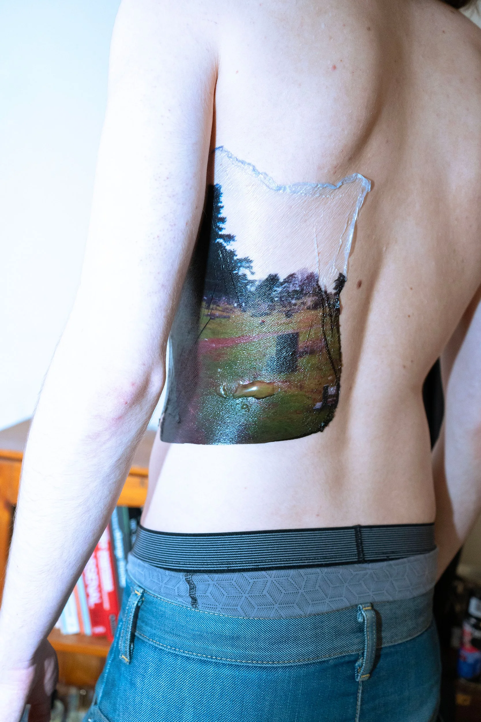 A person with a large, detailed tattoo of a landscape scene on their side, extending from the ribcage to the waist, wearing a striped waistband.