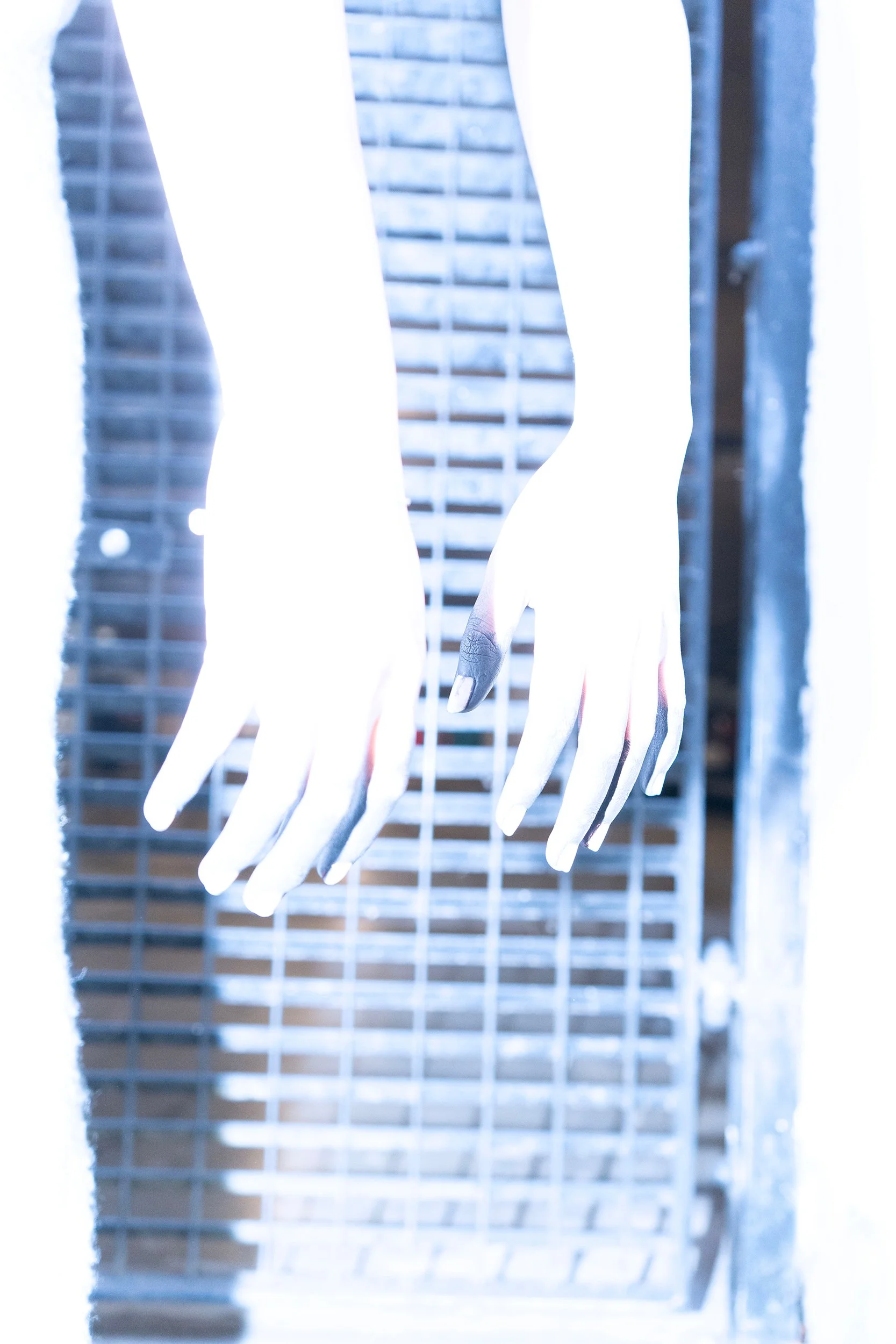 Close-up of white mannequin hands and fingers hanging in front of a wire mesh background, with bright lighting.