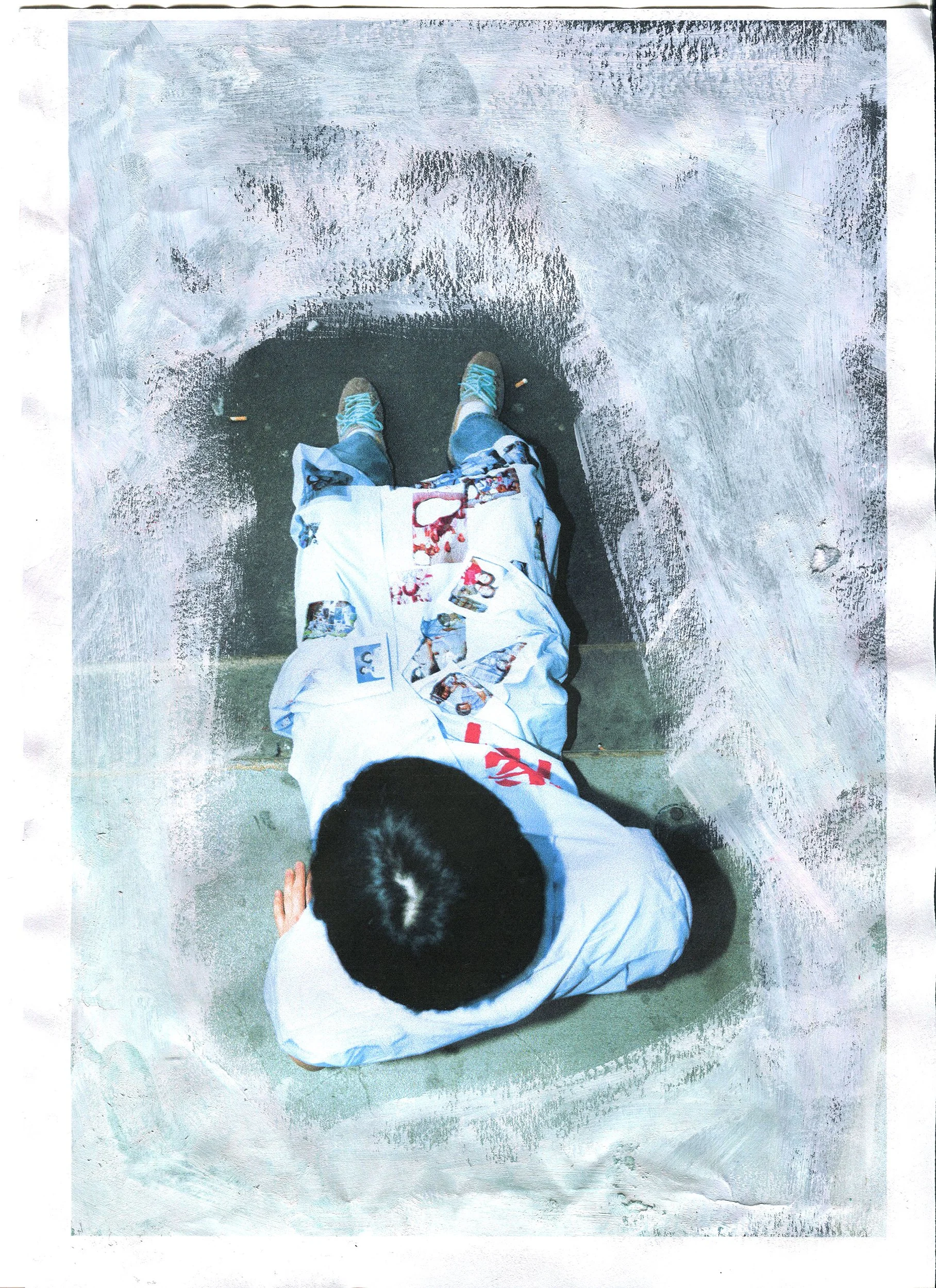 A person in a white jacket with various printed images, including cartoon characters, is sitting on the ground. The photo is taken from above, showing the person's head, shoulders, and legs, along with the ground beneath them.