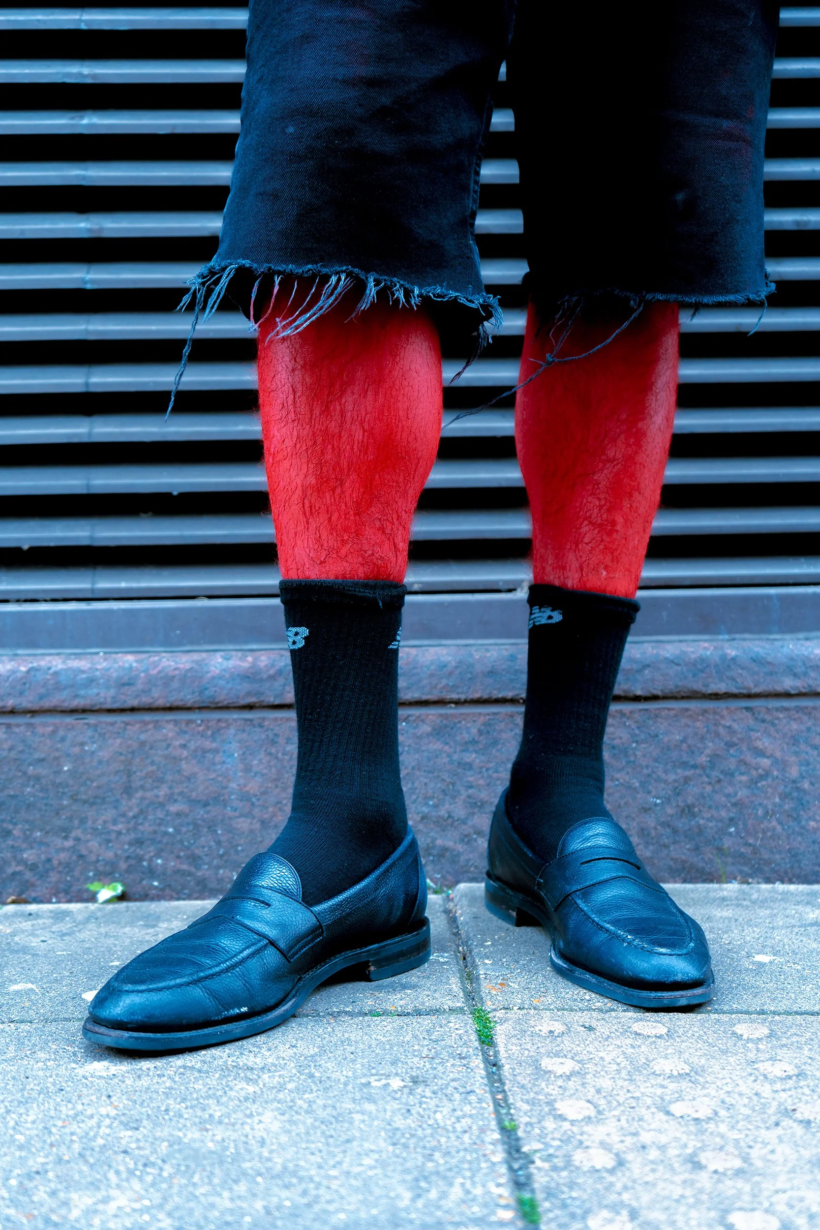 Person sitting on stairs with ripped jeans, red tights, black socks, and black dress shoes.