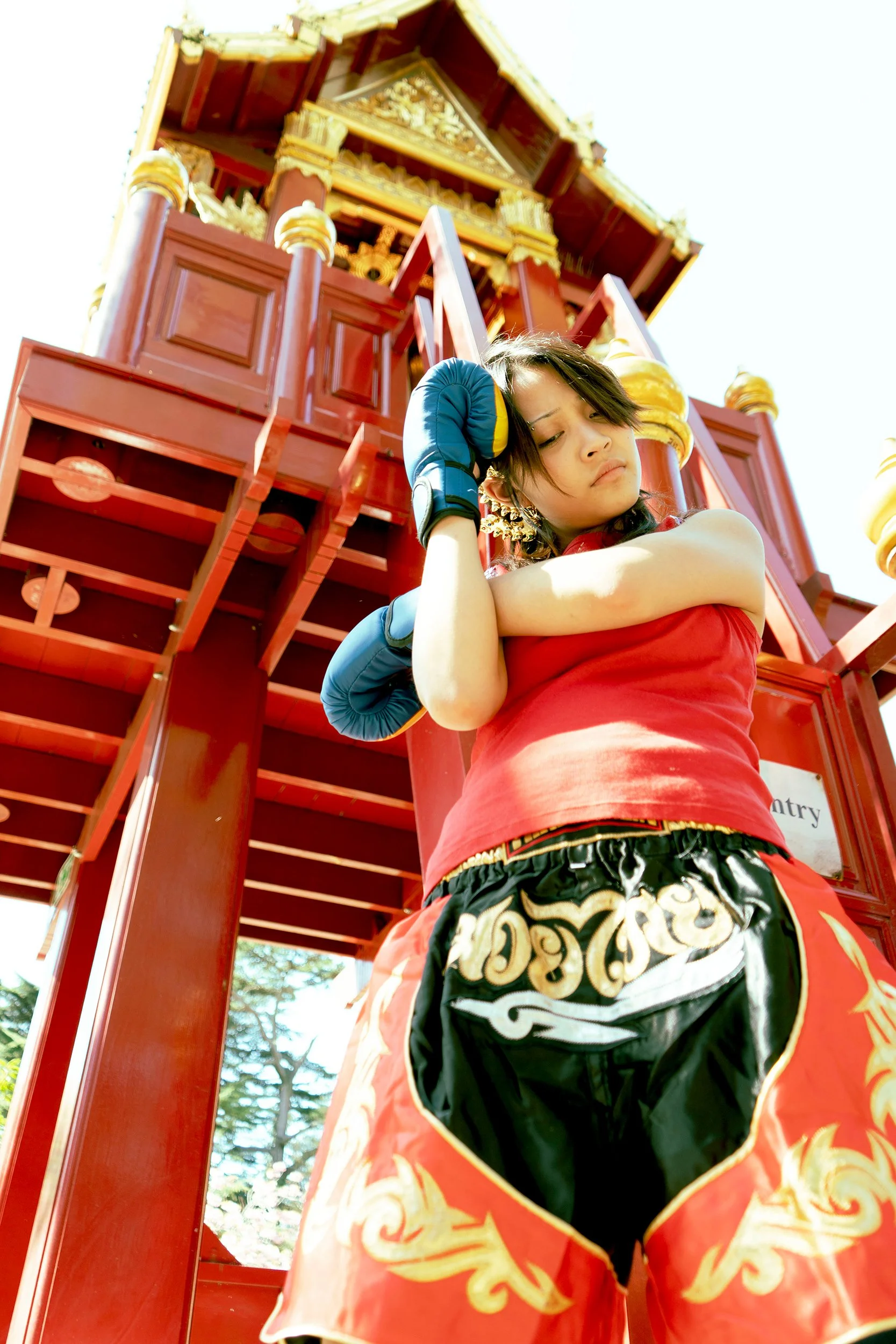A woman dressed in traditional Thai costume, standing in front of a beautiful, ornate temple structure with red and gold details.