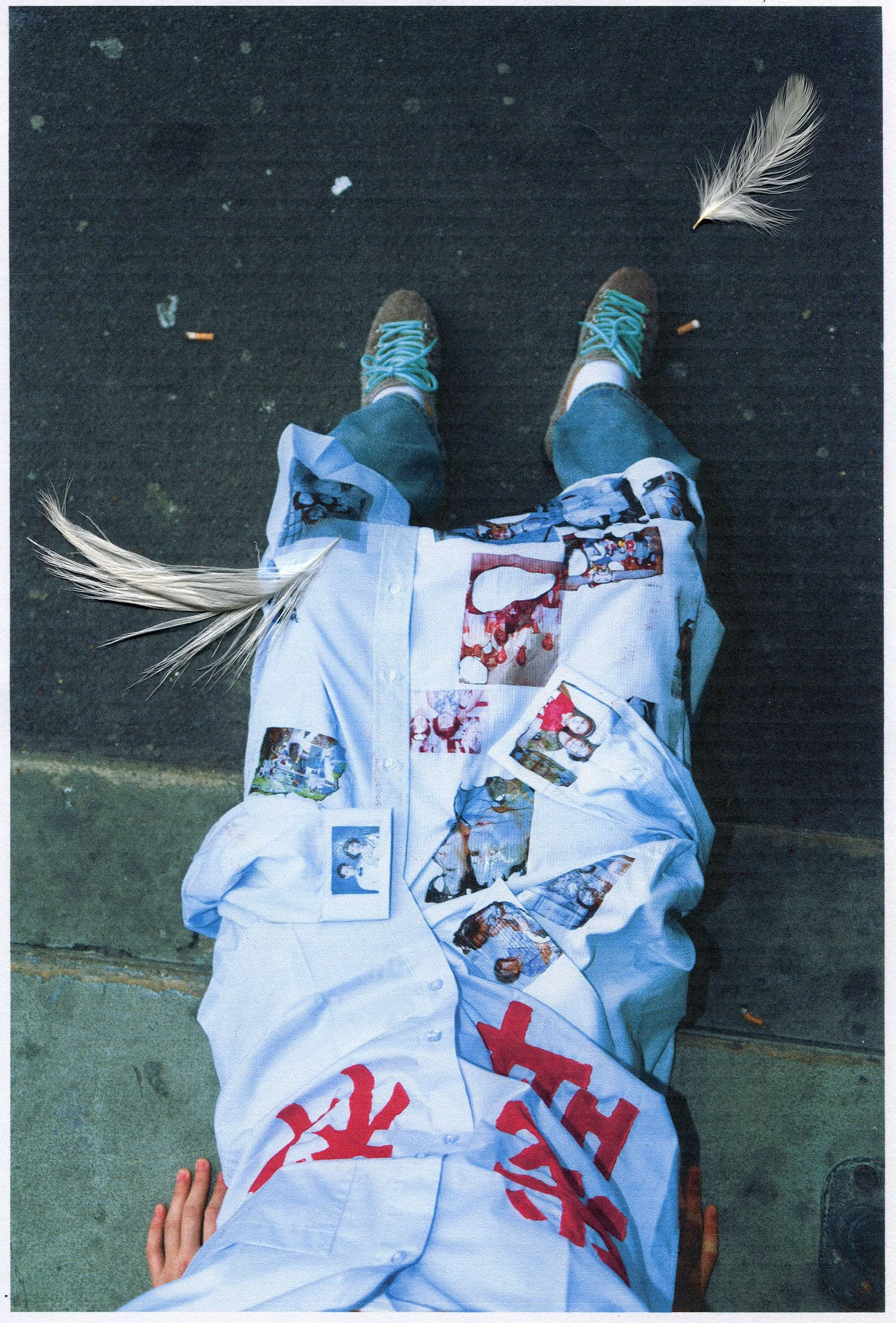 A person lying on the ground wearing a white shirt with images and red Japanese characters, blue pants, and tan shoes with teal shoelaces. Two white feathers and a cigarette are on the ground nearby.