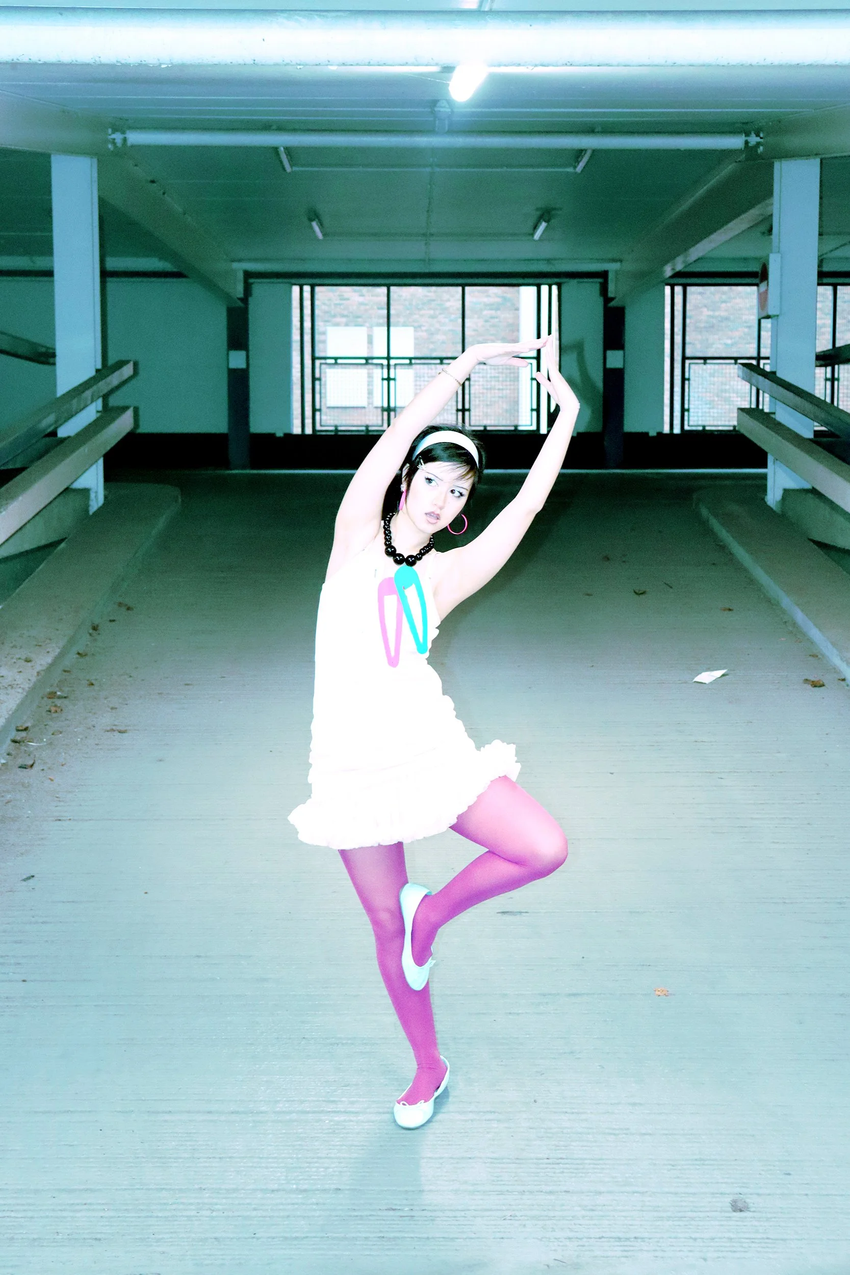 Young woman in colorful outfit performing ballet pose in parking garage