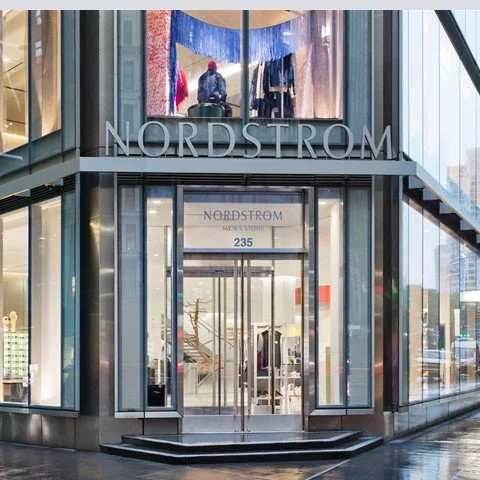 Exterior view of Nordstrom men's store entrance with glass doors, signage, and interior displays visible through the windows.