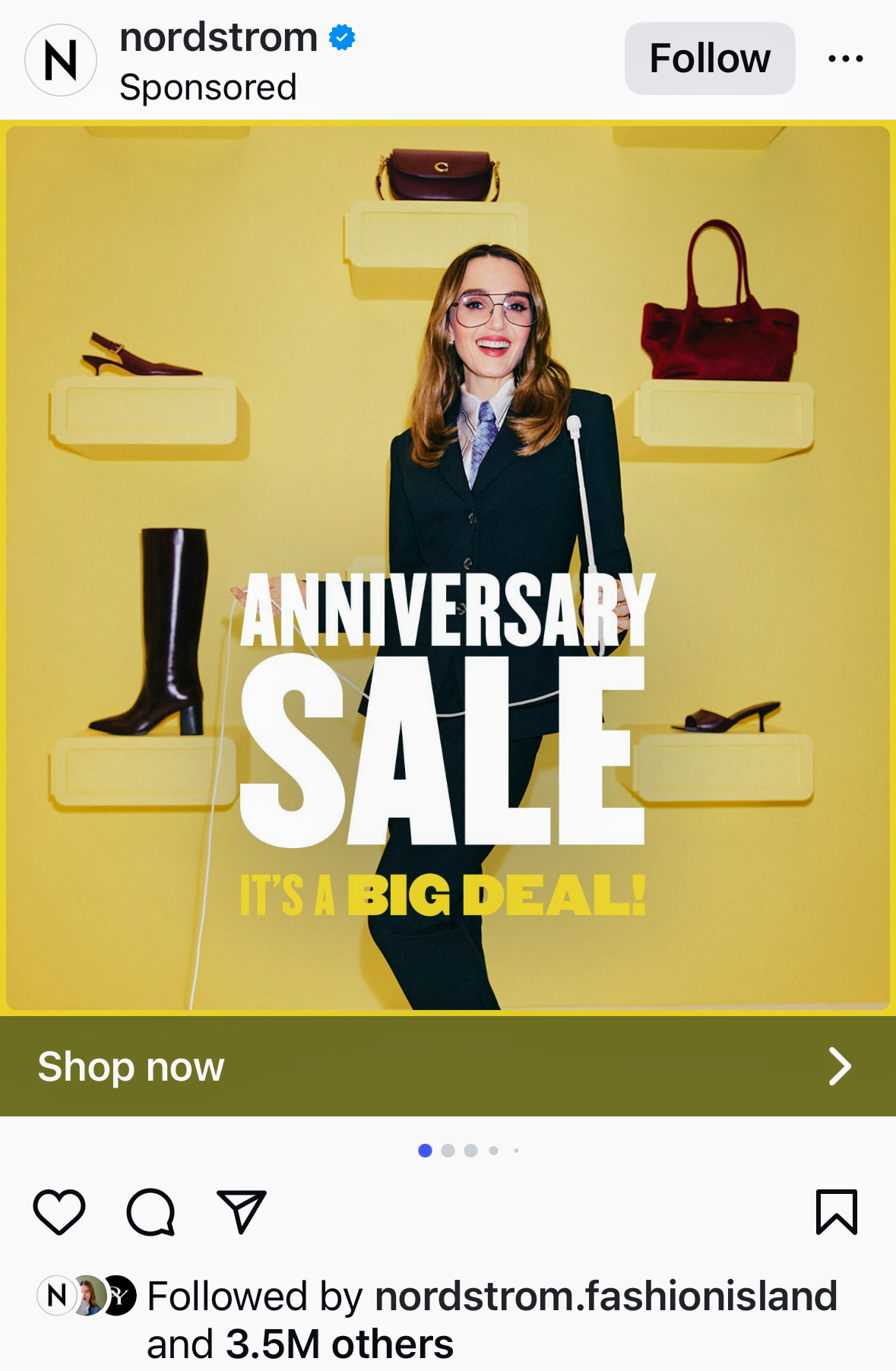 Woman in business suit with glasses smiling at a sale event with yellow background, featuring shelves of shoes and handbags, promoting anniversary sale with bold text.