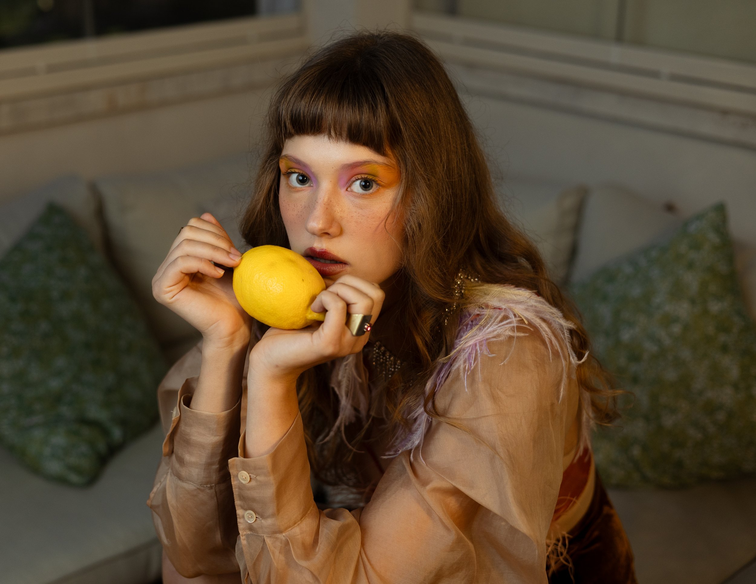 Ragazza con trucco artistico sui occhi di colore giallo, arancione e rosa, che tiene in mano un limone.