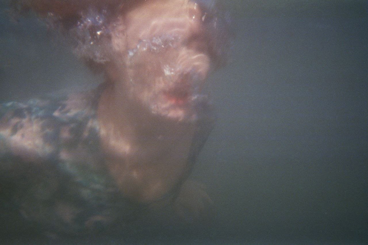 Una persona immersa in acqua, visibile solo il volto e parte del busto, con conseguente riflesso e distorsione dell'immagine