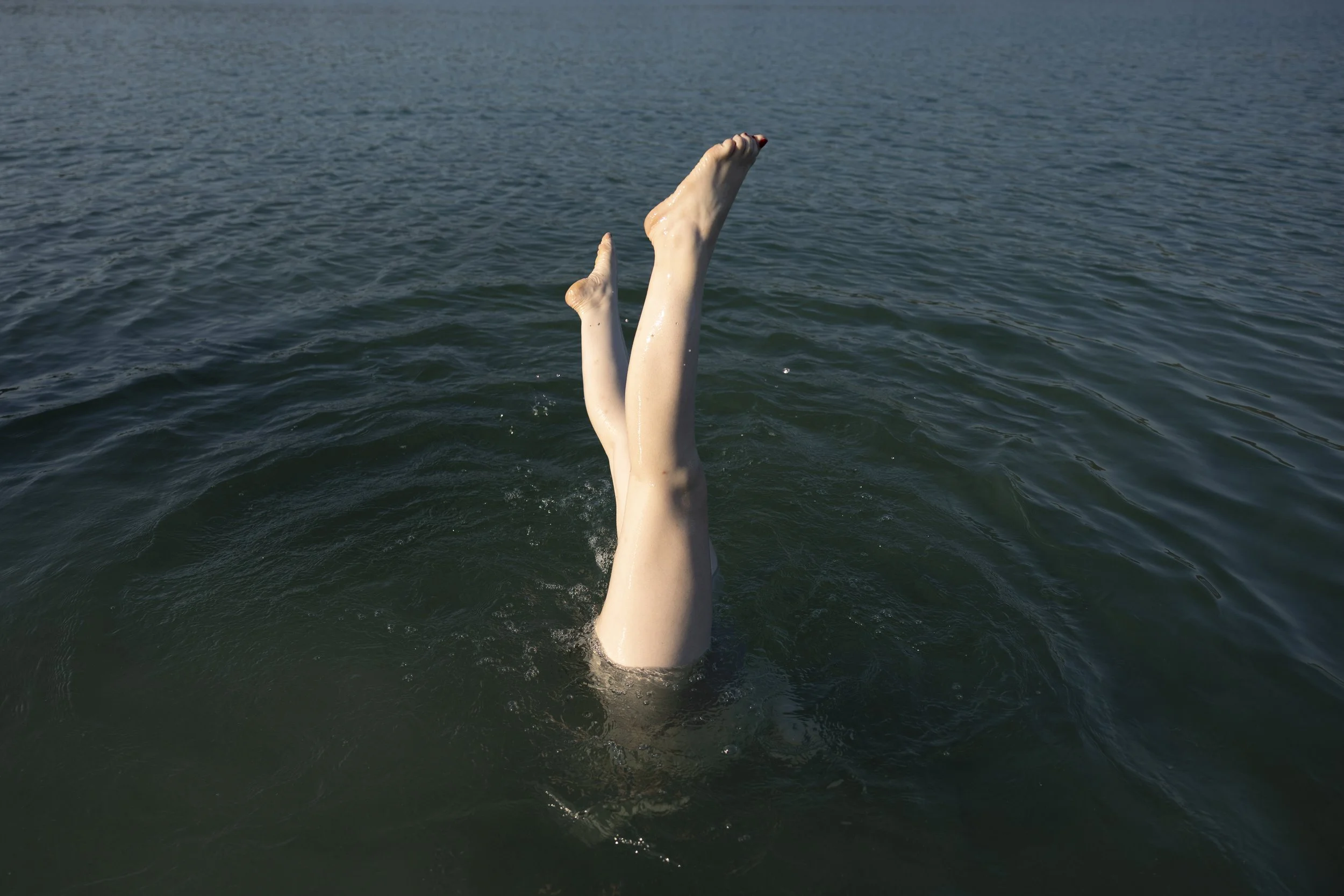Una persona che si tuffa in un lago, con solo le gambe e le braccia visibili sopra l'acqua.