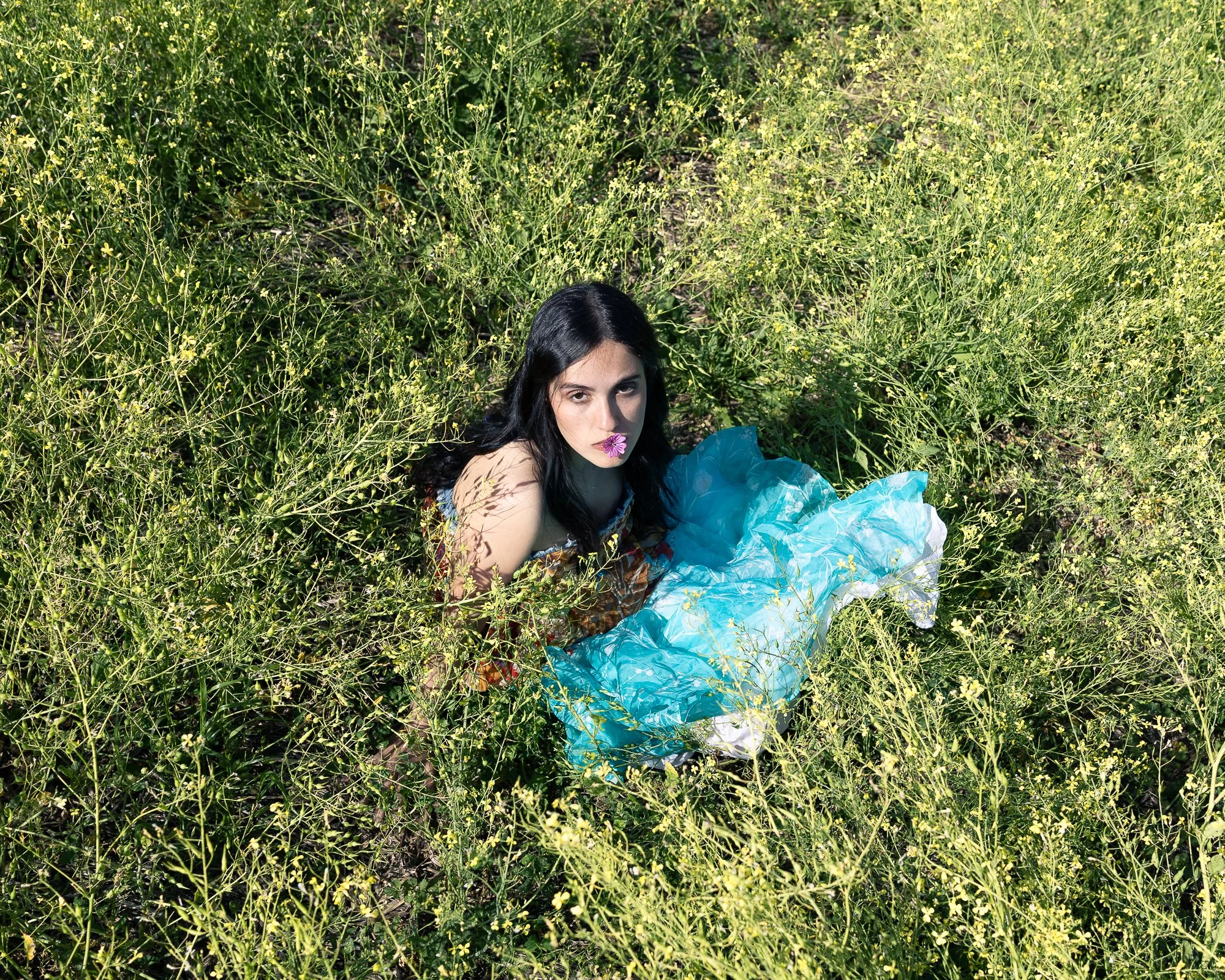 Donna con capelli neri e vestito colorato sdraiata tra i fiori gialli in un campo