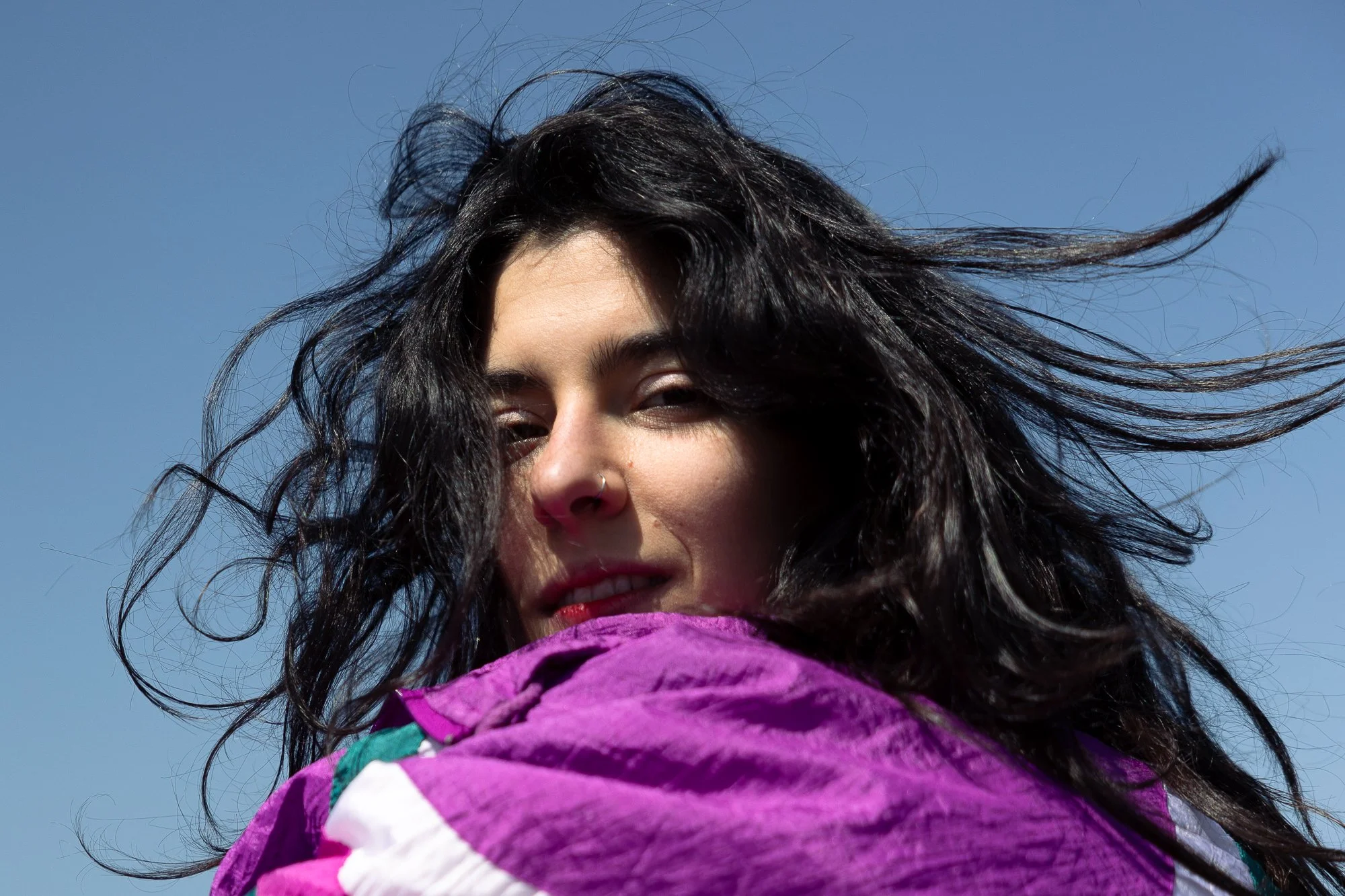 Ragazza con capelli mossi neri e occhi chiusi si copre la bocca con un foulard viola