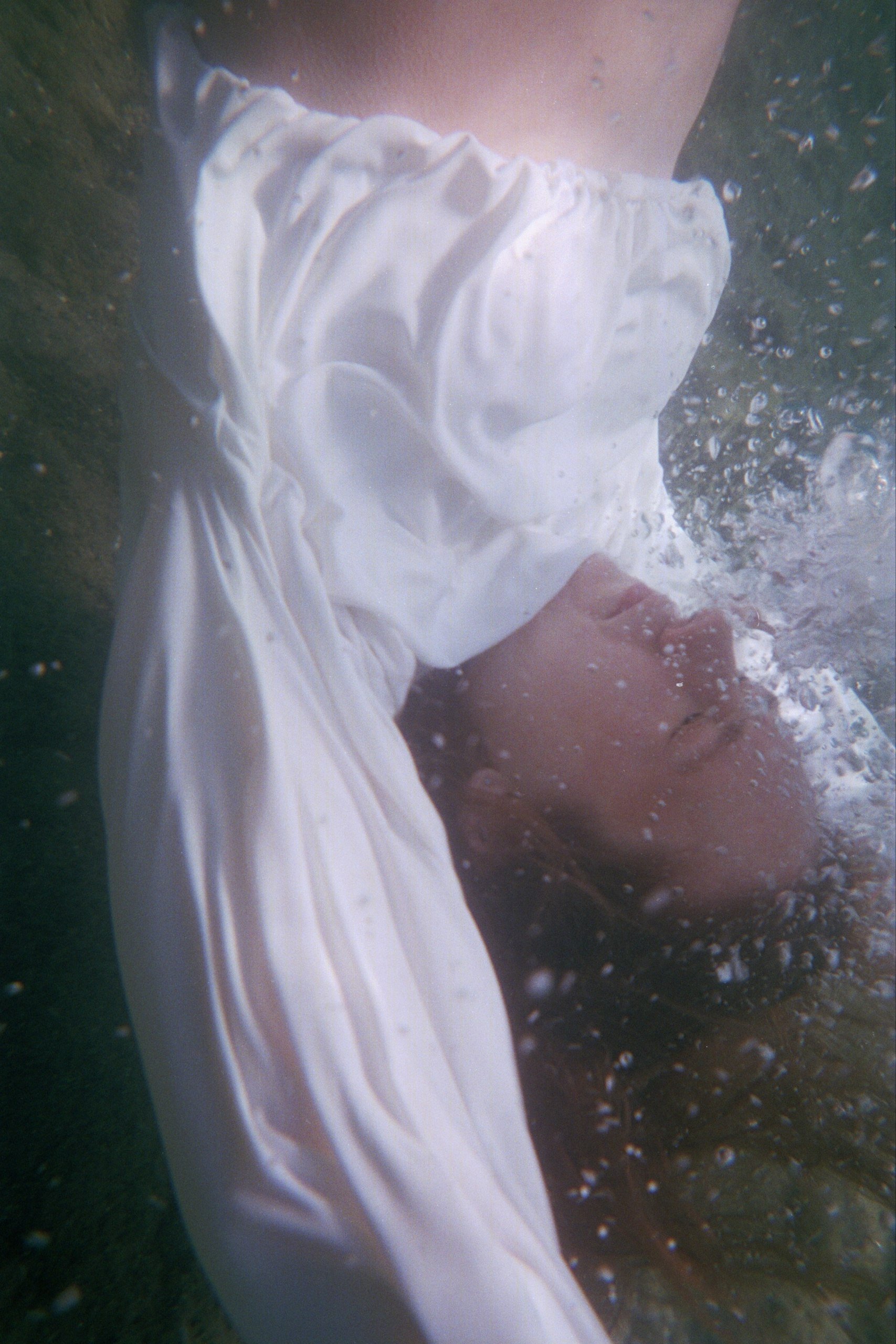 Una persona in piedi sulla riva di una spiaggia con un vestito bianco, vicino all'acqua del mare e alla sabbia.