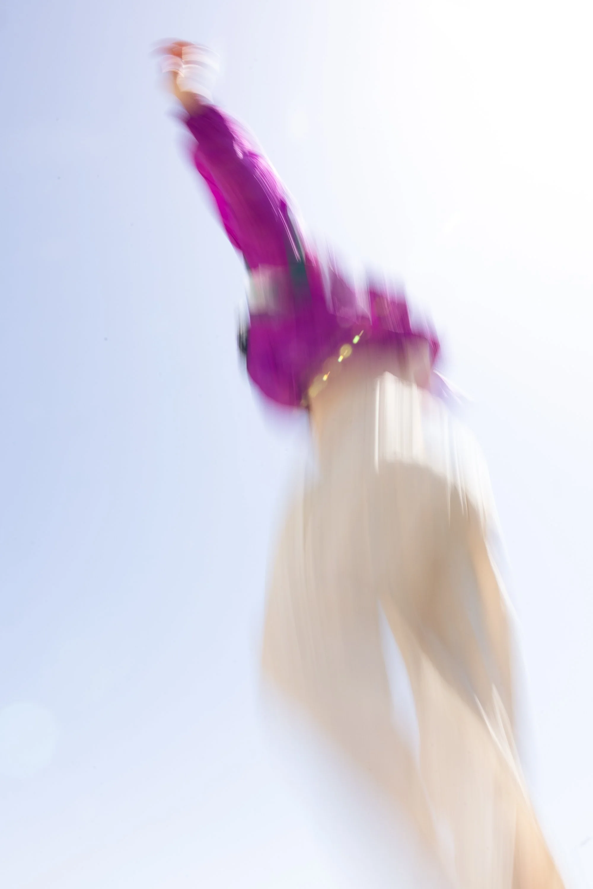Persona che si tuffa o cade dall'alto, vestita con un completo rosa e pantaloni beige, visibile contro il cielo chiaro.