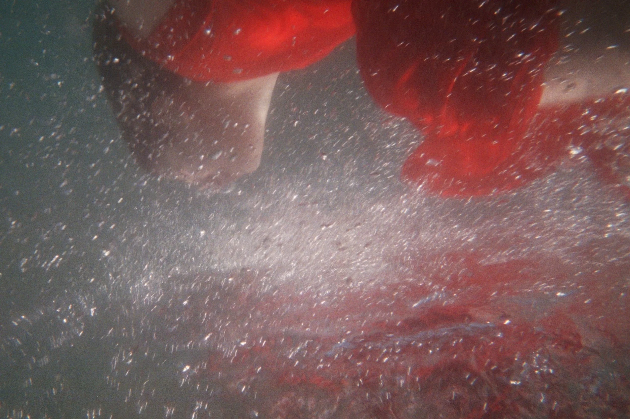 Immagine sott'acqua con bolle d'acqua e un oggetto rosso che sembra essere un cappello o un tessuto.