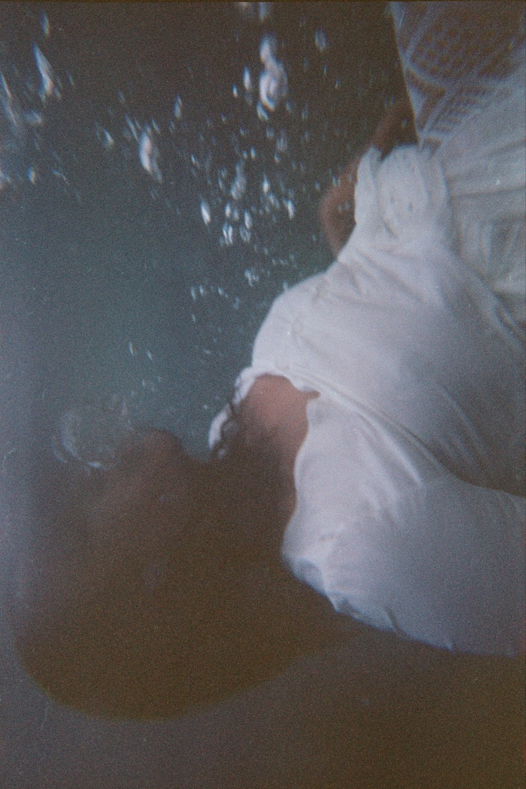Una persona con camicia bianca versa un liquido da una bottiglia in un bicchiere di plastica trasparente, creando alcune gocce d'acqua nell'aria.