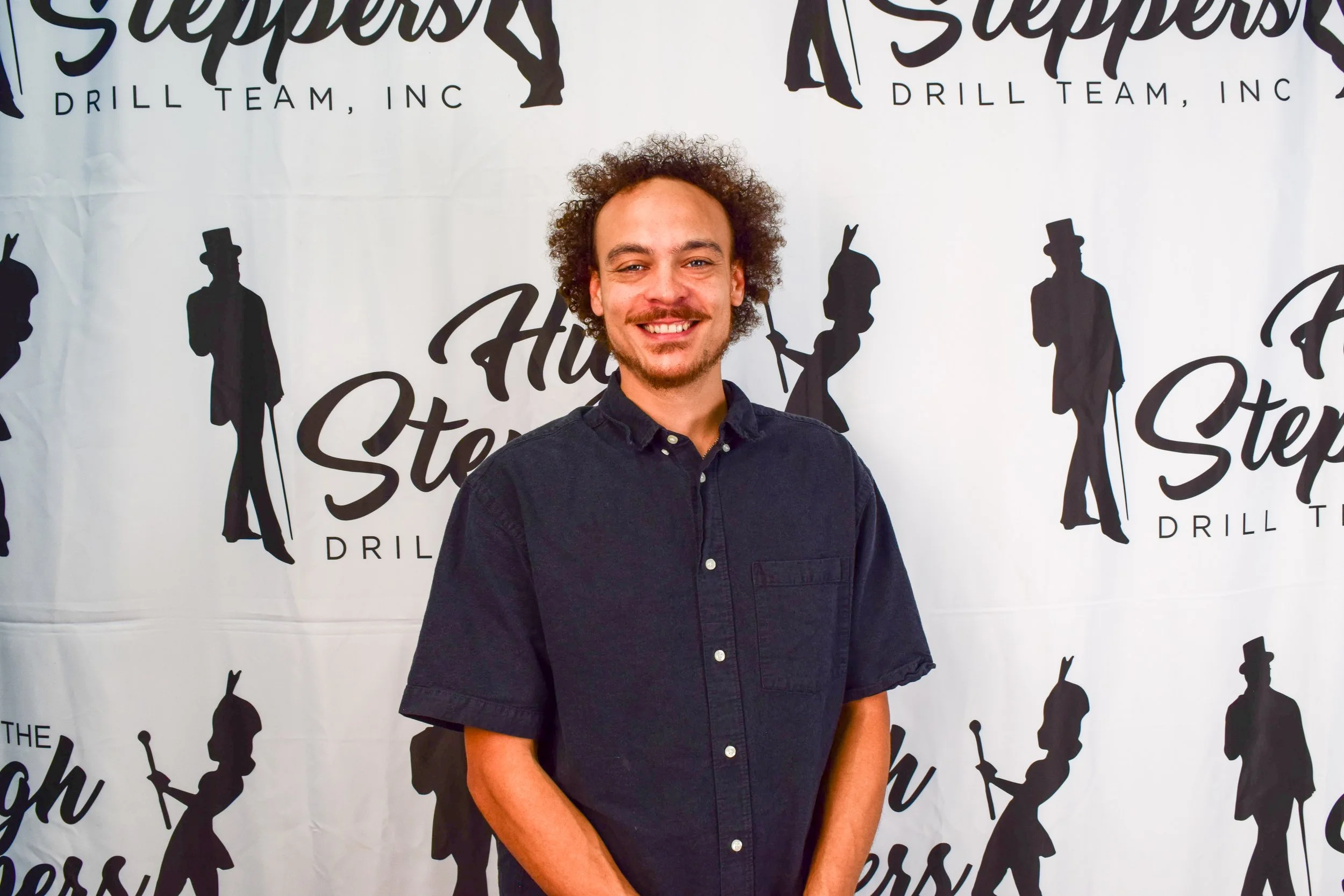 A man with curly hair and a beard smiling, wearing a dark button-up shirt, standing in front of a backdrop with silhouettes of people holding tools and the text 'The Southern Drillers'.