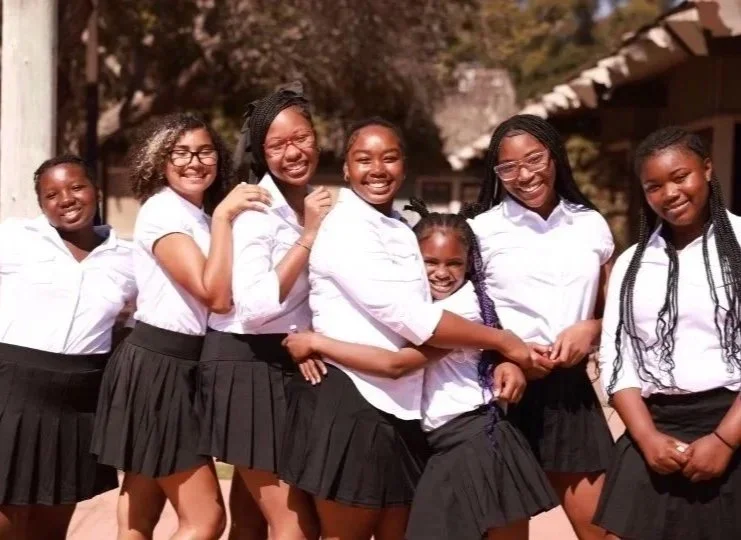 Group of seven High Steppers in uniforms standing outdoors and smiling for a photo.