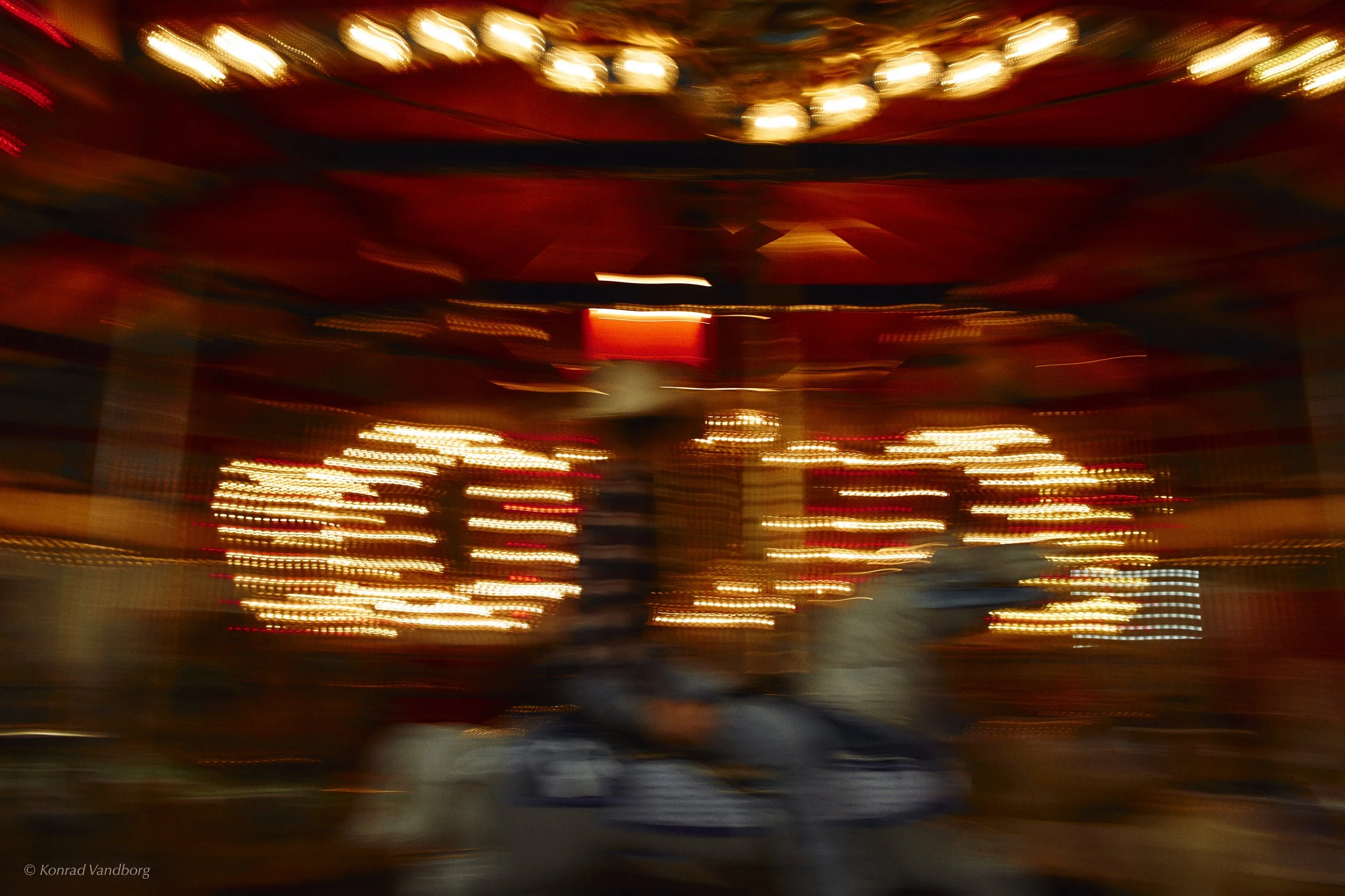 Blurred image of a carnival ride with bright lights in motion, creating streaks of yellow, red, and blue.