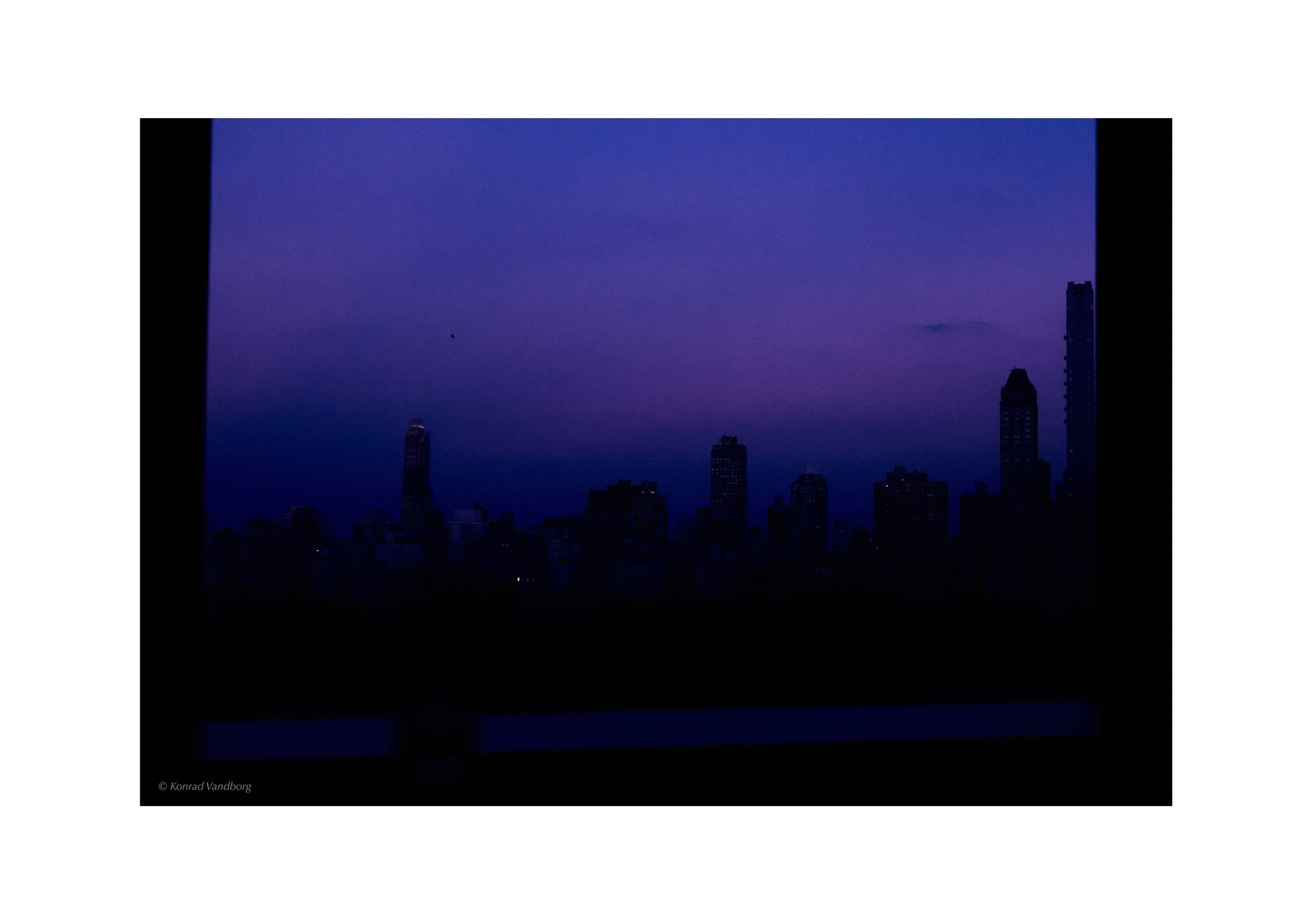 Nighttime city skyline with tall buildings and purple-blue sky.