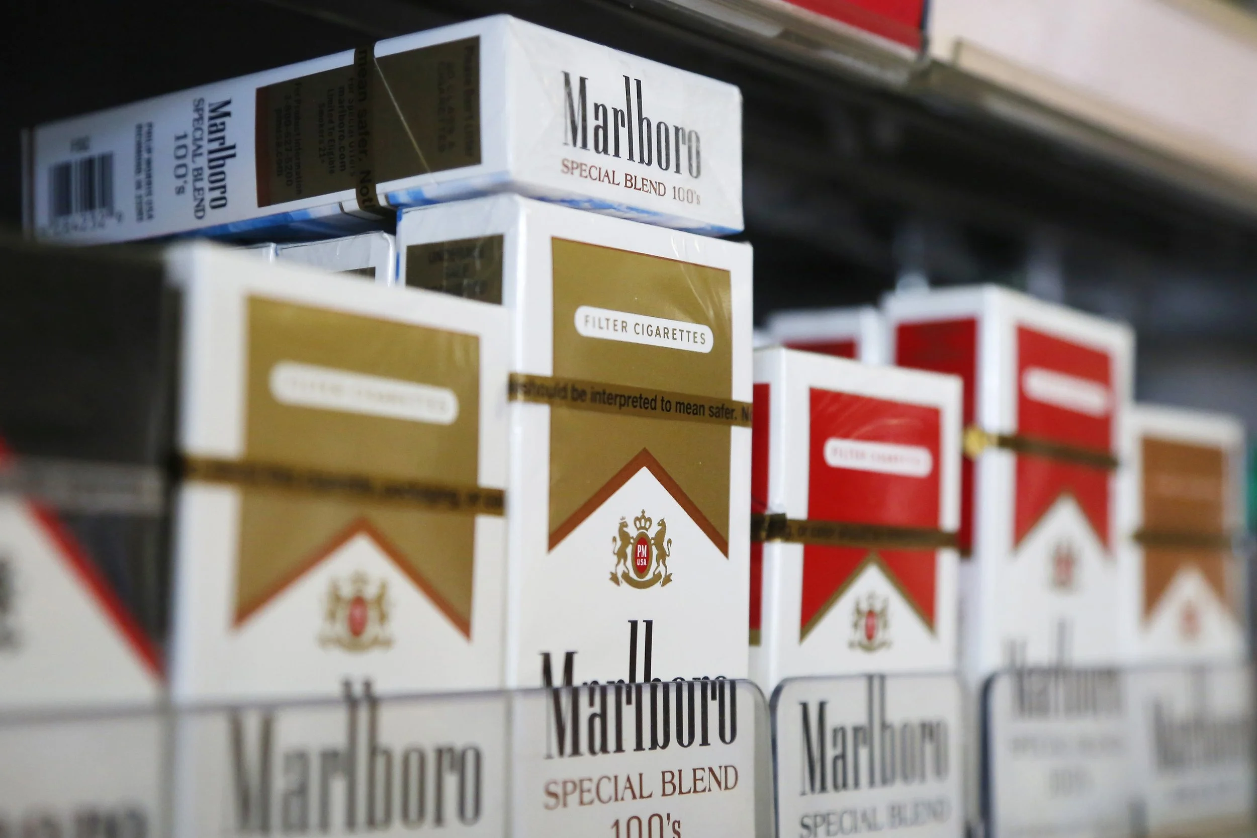 Close-up of cigarette packs on a store shelf, featuring Marlboro Special Blend 100's and other brands.