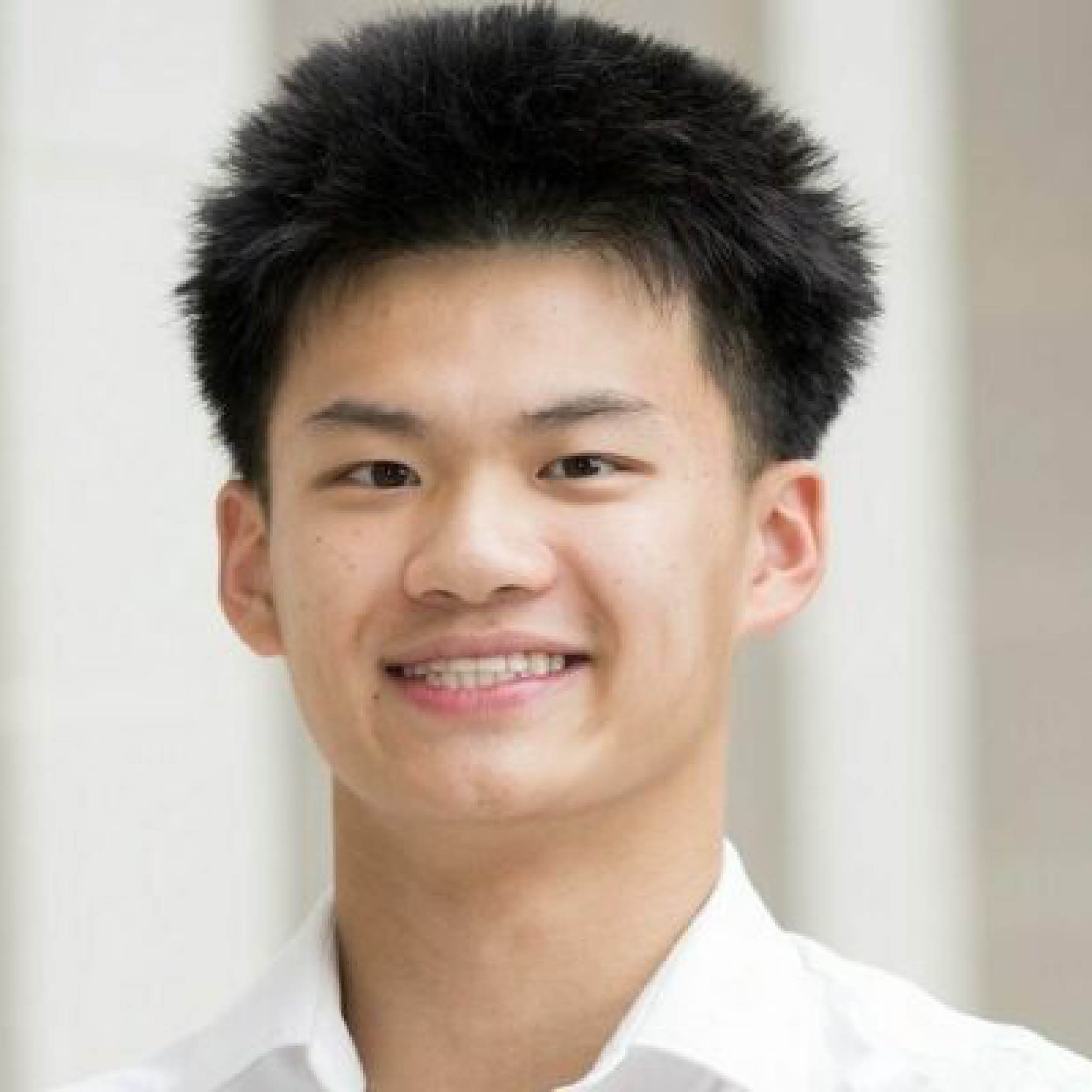 A man with short, spiky black hair and light skin, smiling with visible teeth, wearing a white shirt.