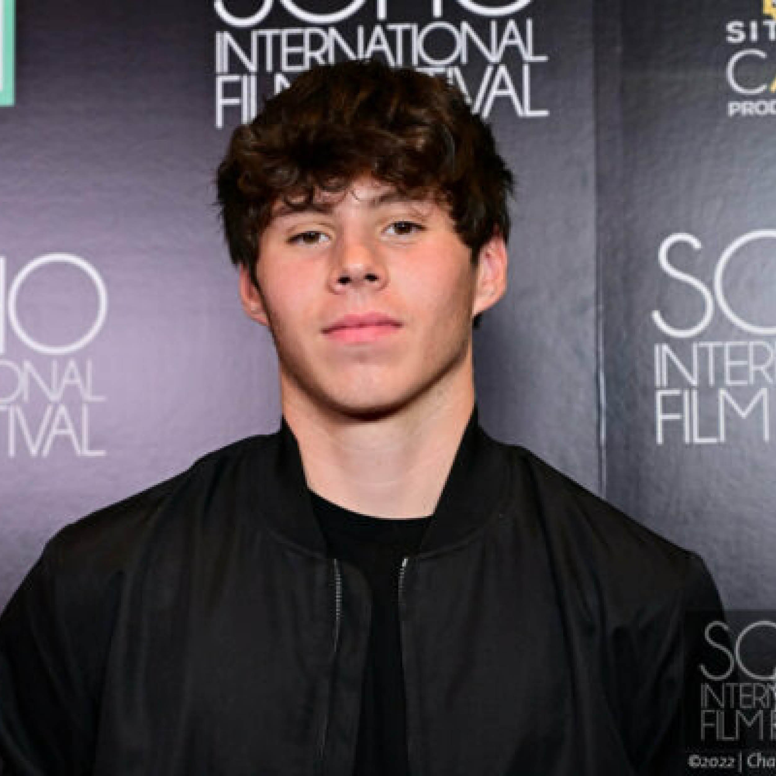A man with dark, curly hair in front of a background with text related to an international film festival.