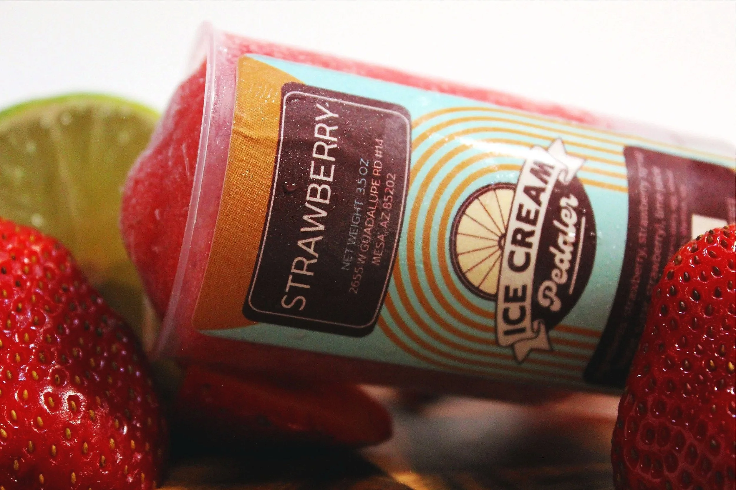 Close-up of a Strawberry sorbet push pop surrounded by fresh strawberries and a slice of lime.