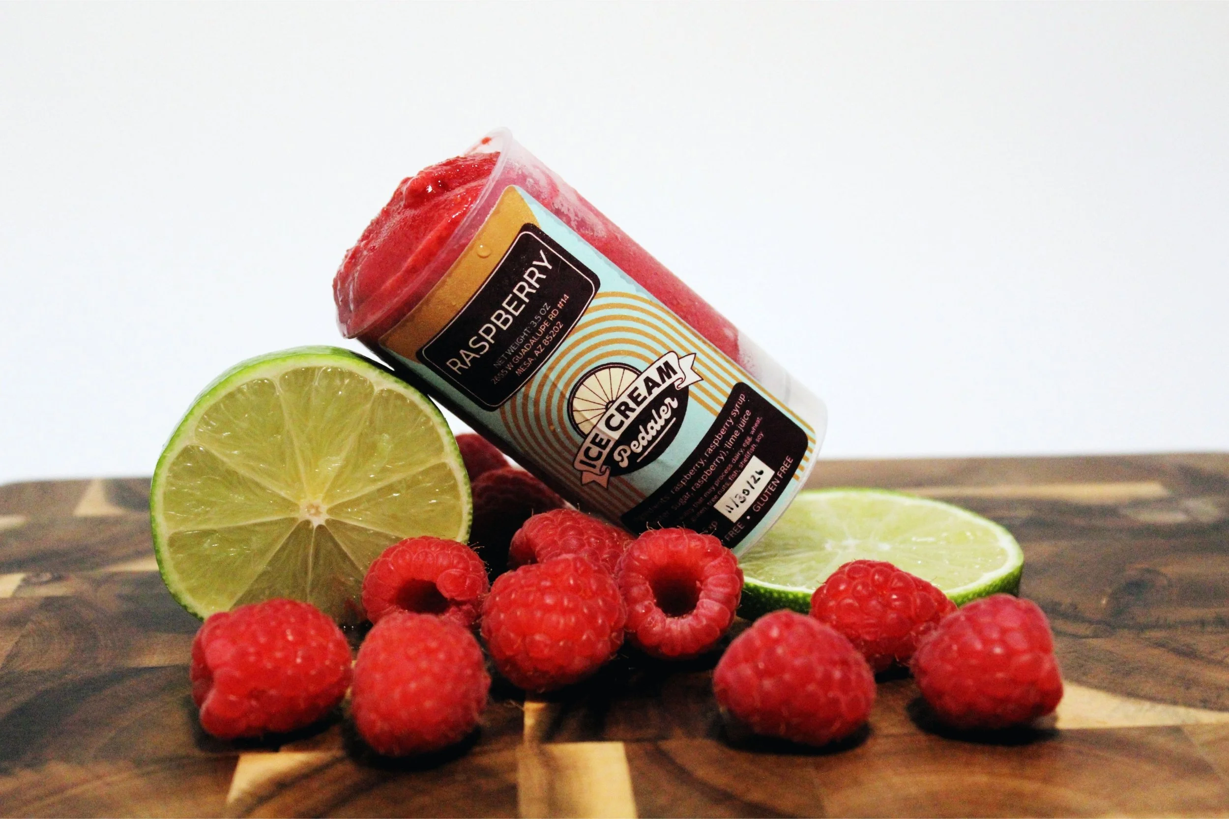 Fresh raspberries, lime slices, and a raspberry sorbet push pop on a wooden surface.