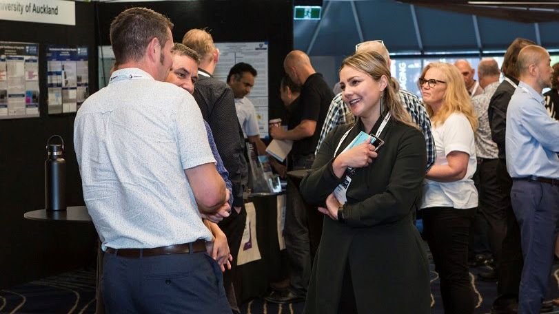 Group of people at a professional conference or networking event, engaging in conversation and looking at displays.
