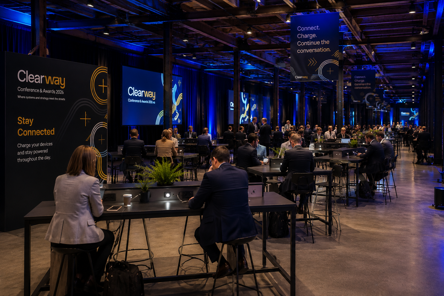 Conference attendees seated at the Clearway Workzone Hub at tables with laptops.