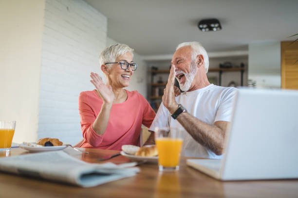 An elderly couple laughing and giving each other a high-five at a breakfast table after getting a reverse mortgage