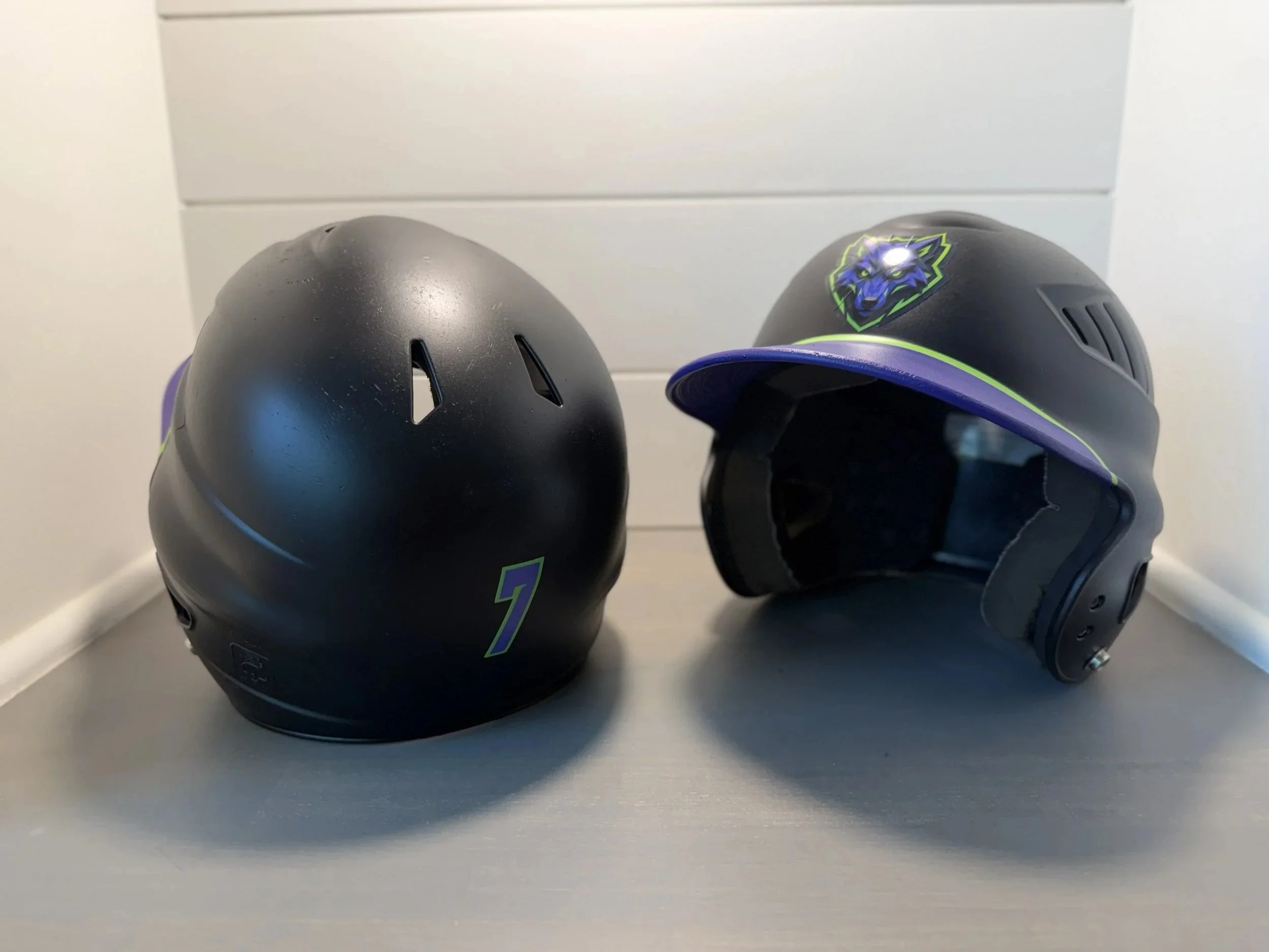 Two black motorcycle helmets with green and purple accents, one with a wolf logo, placed on a white surface against a white background.