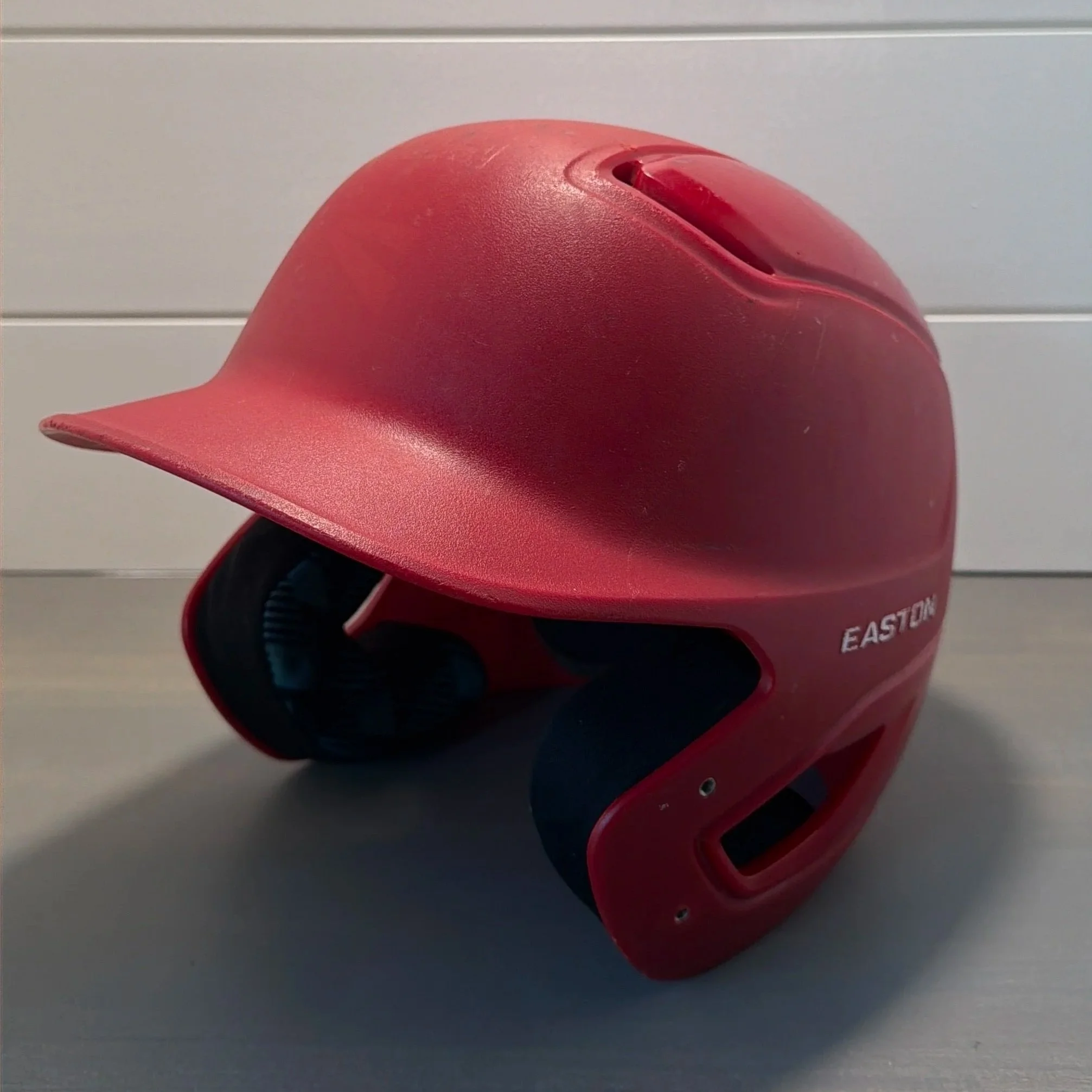 Red plastic object with a curved shape and two slots on the top, labeled 'EASTON', placed on a surface with a gray background.