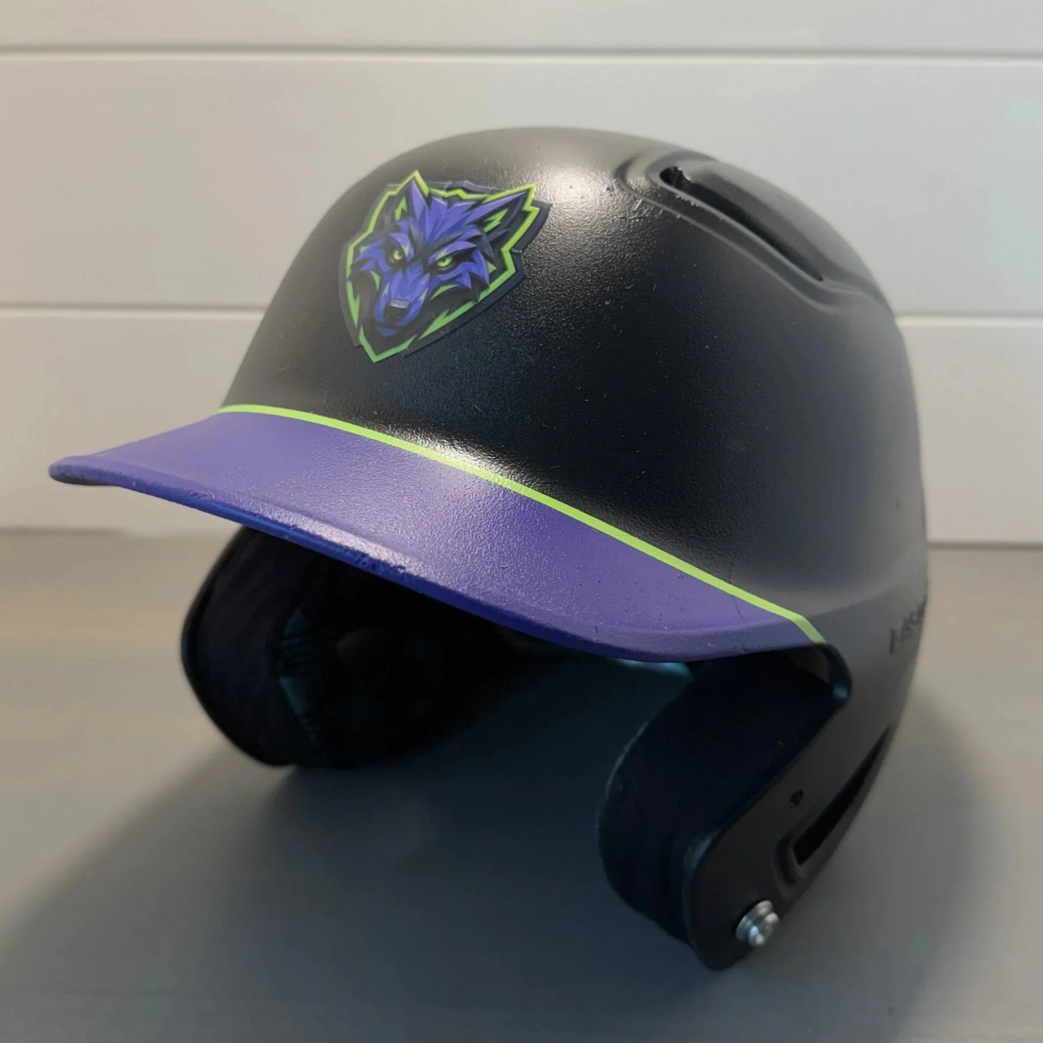 Close-up of a black helmet with a wolf emblem sticker, placed on a flat surface.