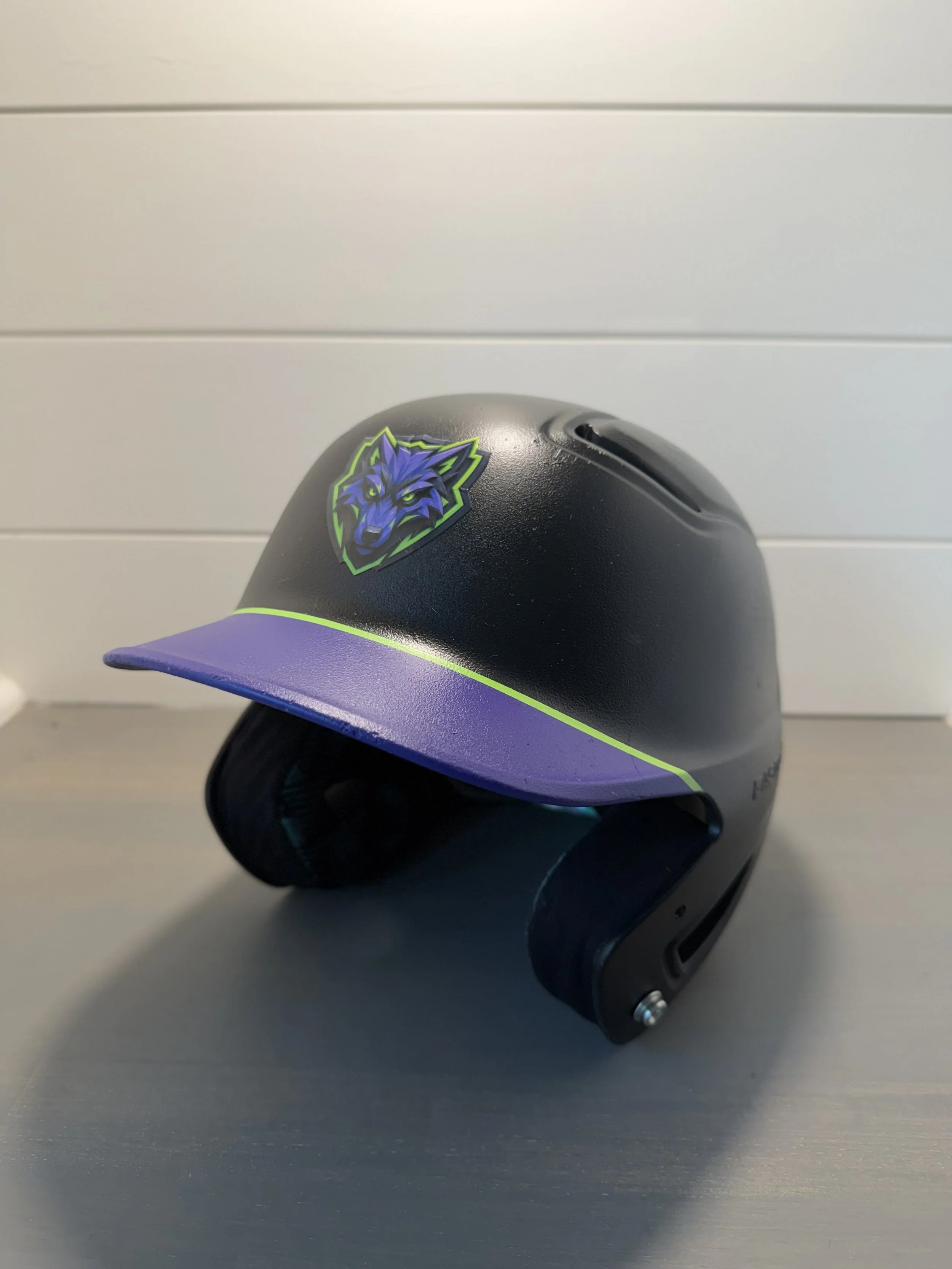 A black helmet with a purple brim and a sticker of a blue wolf head with green eyes and accents.