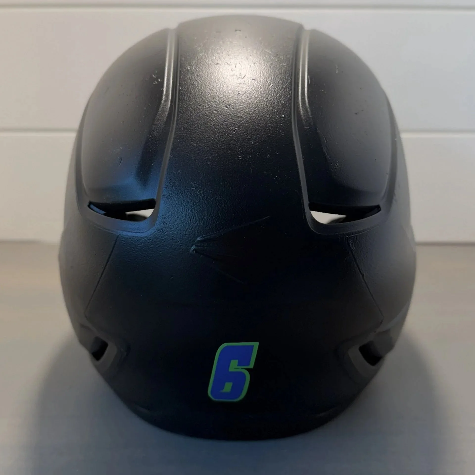 Close-up of a round black Bowling ball with finger holes, resting on a surface with a sticker that has a number 5 in a green box.