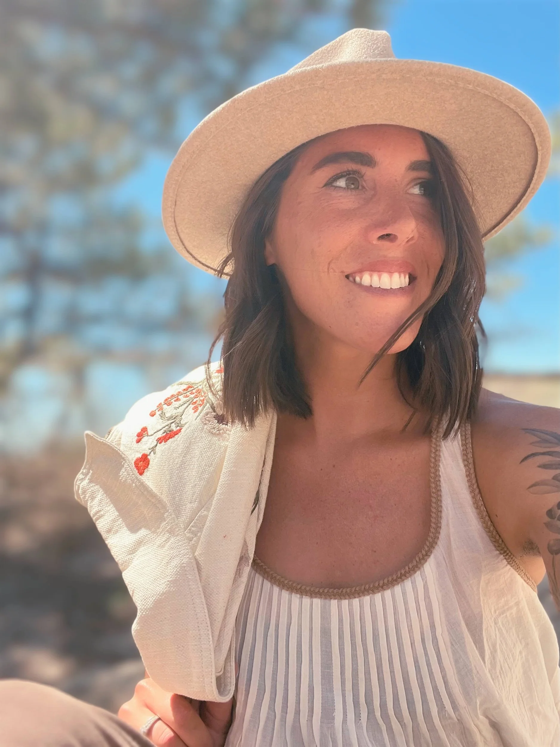Ellen smiling outdoors wearing a wide-brimmed hat and a white, embroidered blouse.